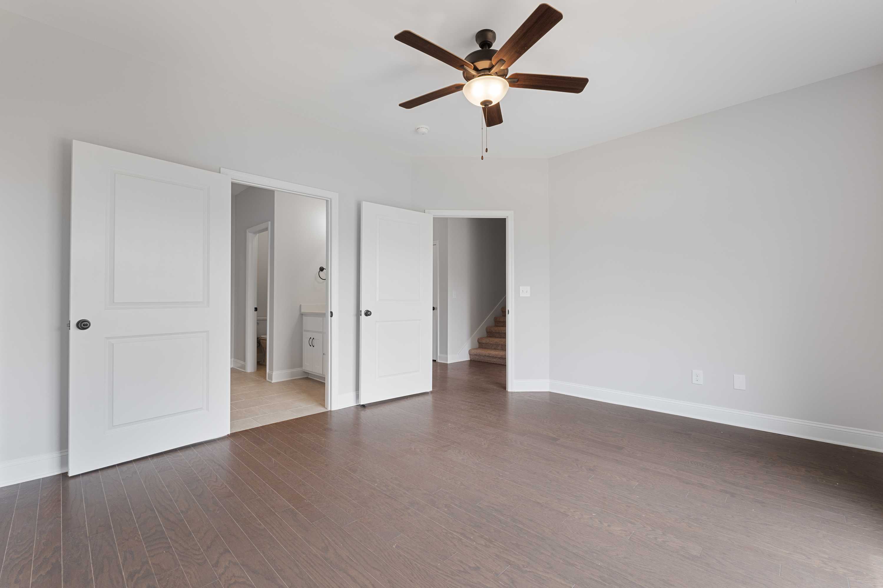 Spacious master suite in The Copeland home design with open double doors, ceiling fan, hardwood floors, and adjacent stairs