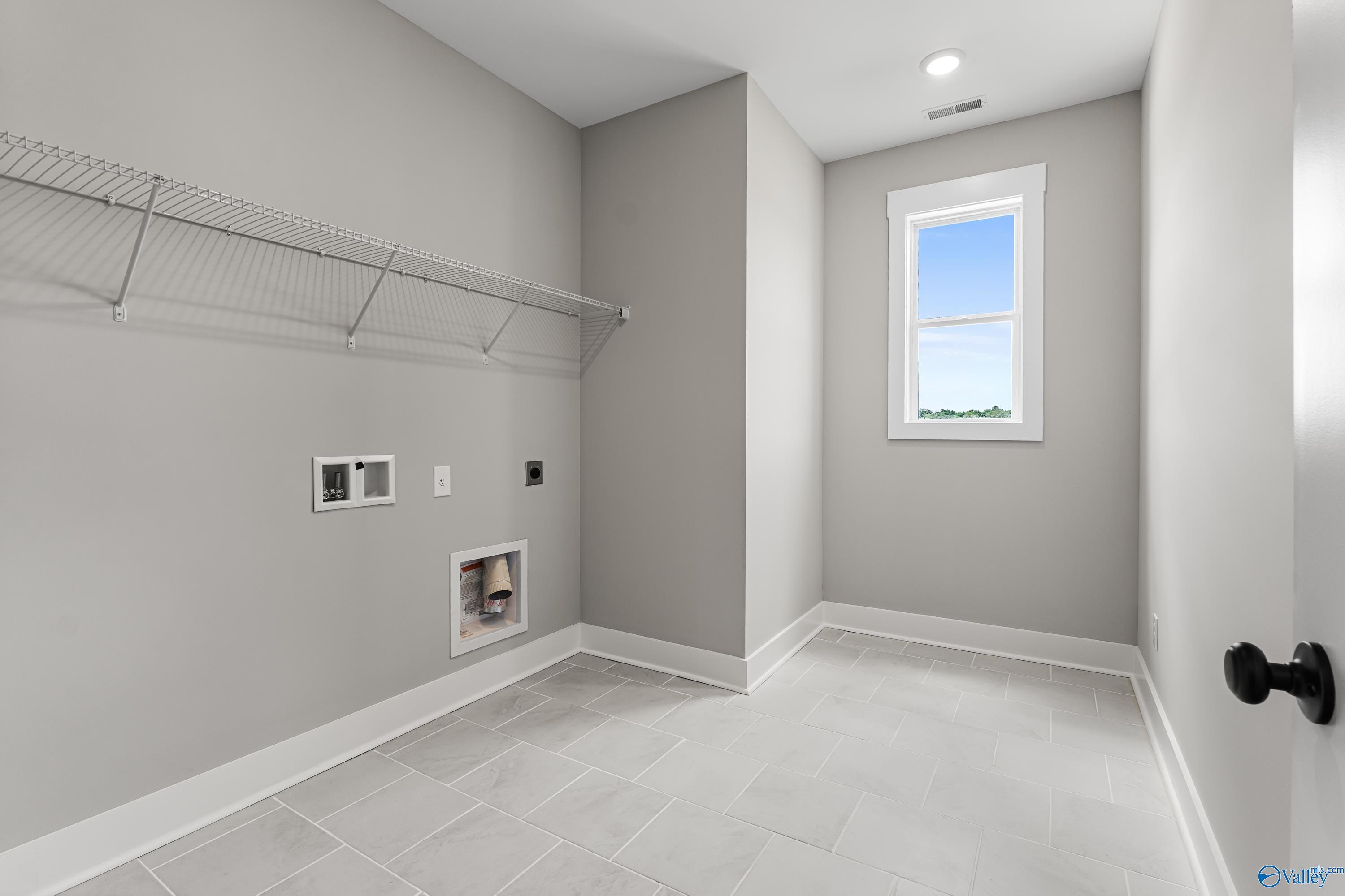 Modern laundry room with wire shelving, washer-dryer hookups, gray walls, tile floor in Davidson Homes The Arcadia, Huntsville AL