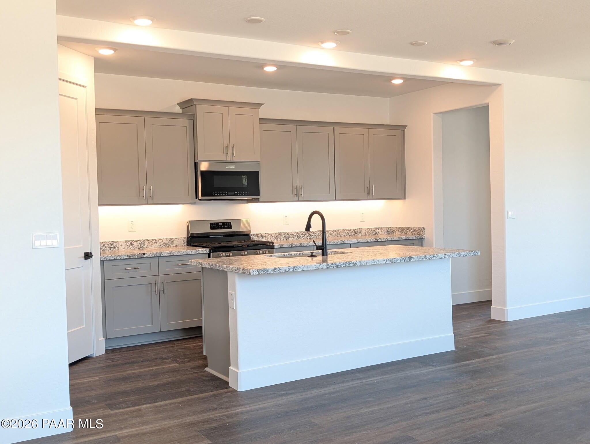 Modern kitchen with grey cabinets, granite island, and stainless appliances in The Frontier II F home, Prescott, Arizona.