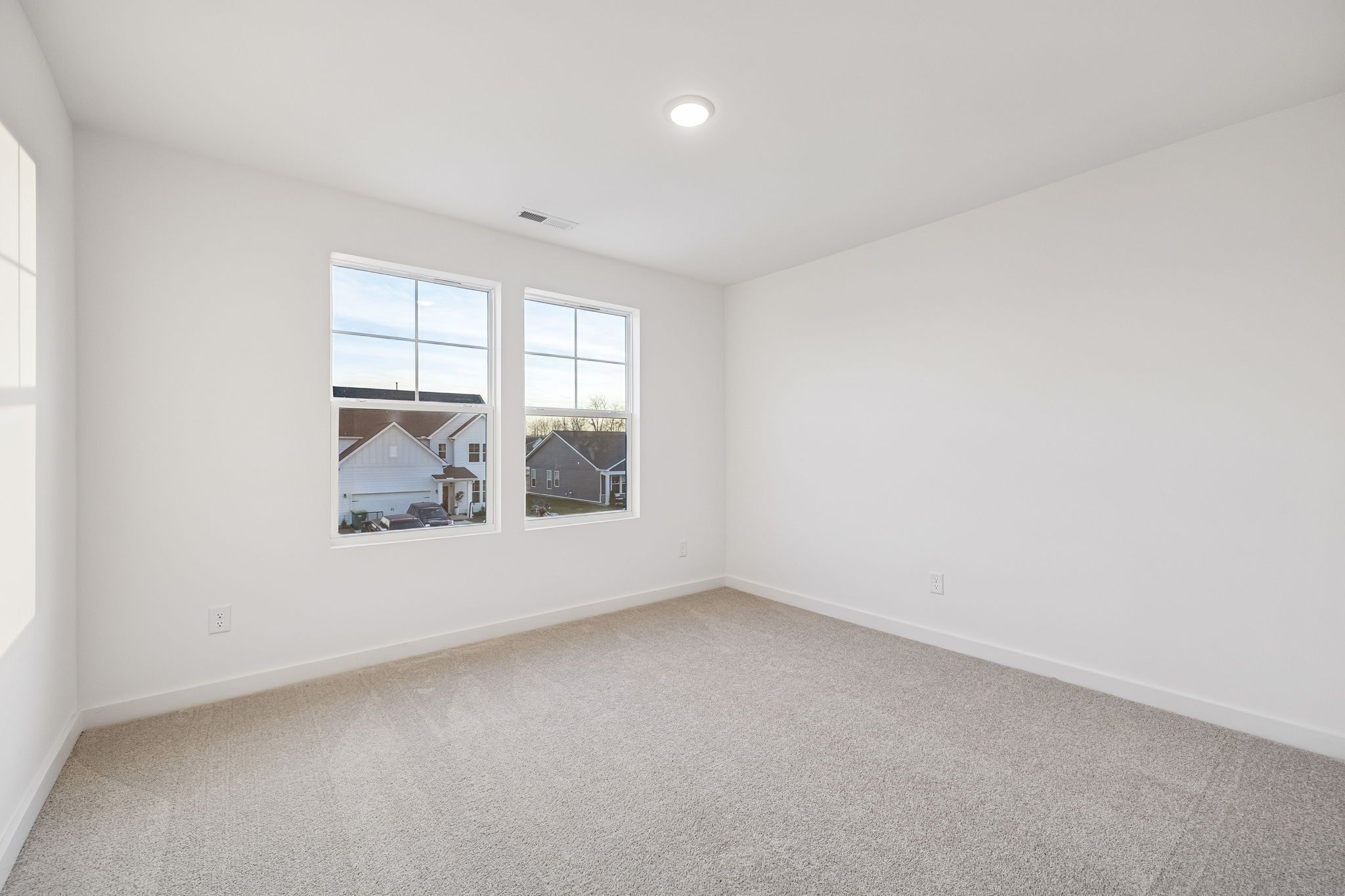 Bright empty bedroom with large windows overlooking neighborhood, white walls, beige carpet in Davidson Homes The Willow