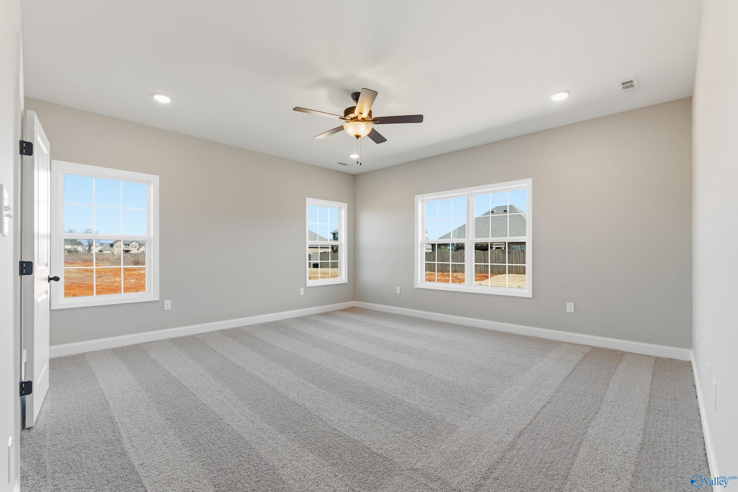 Bright secondary bedroom featuring large windows, ceiling fan, and neutral carpet in Davidson Homes The Finleigh, Meridianville, Alabama