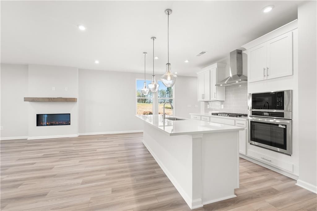 Modern open kitchen with white island, stainless steel appliances, linear gas fireplace in Davidson Homes The Cary A, Winder, GA