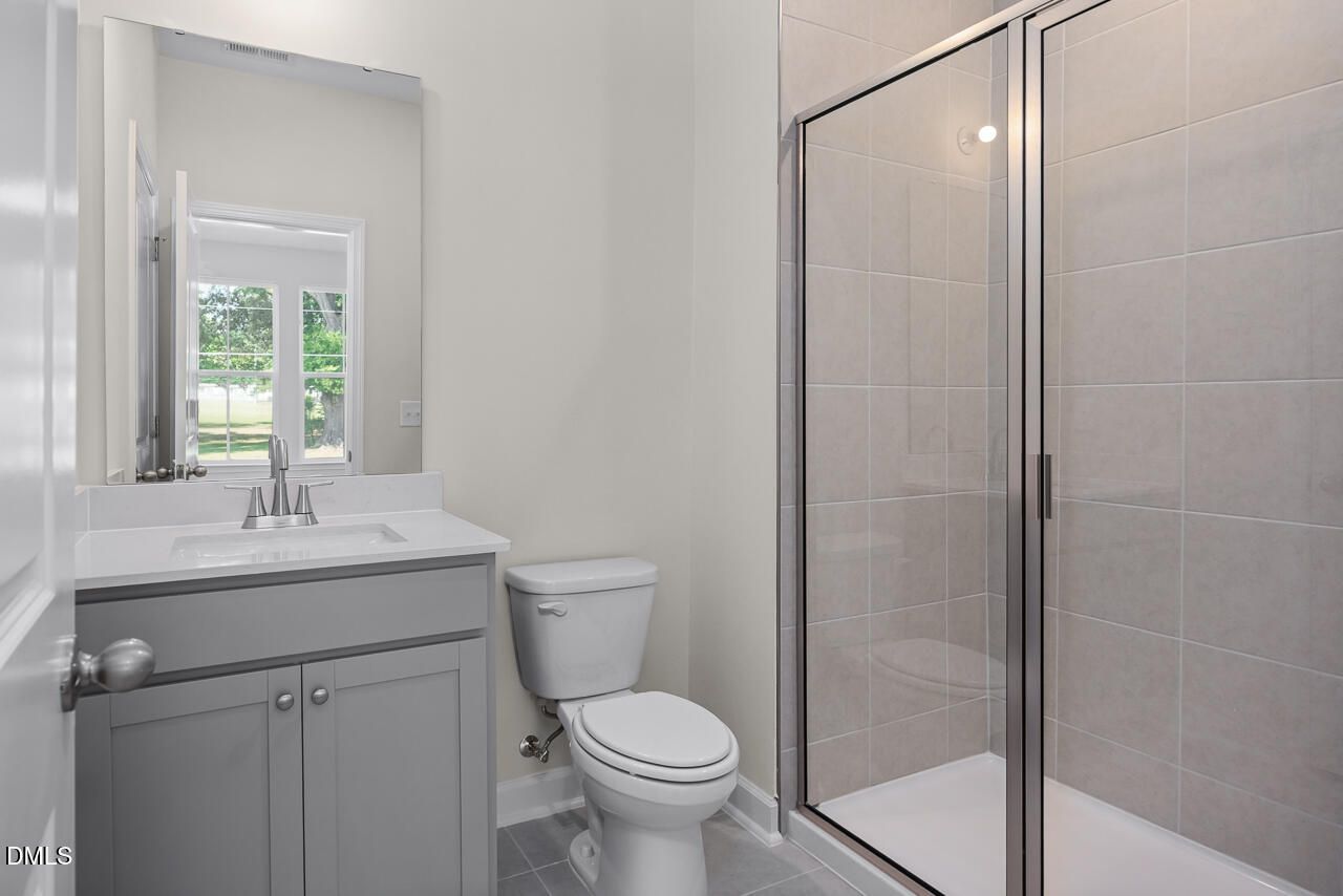 Modern bathroom with grey vanity, white quartz countertop, and glass-enclosed shower in The Mitchell at Camden Park.