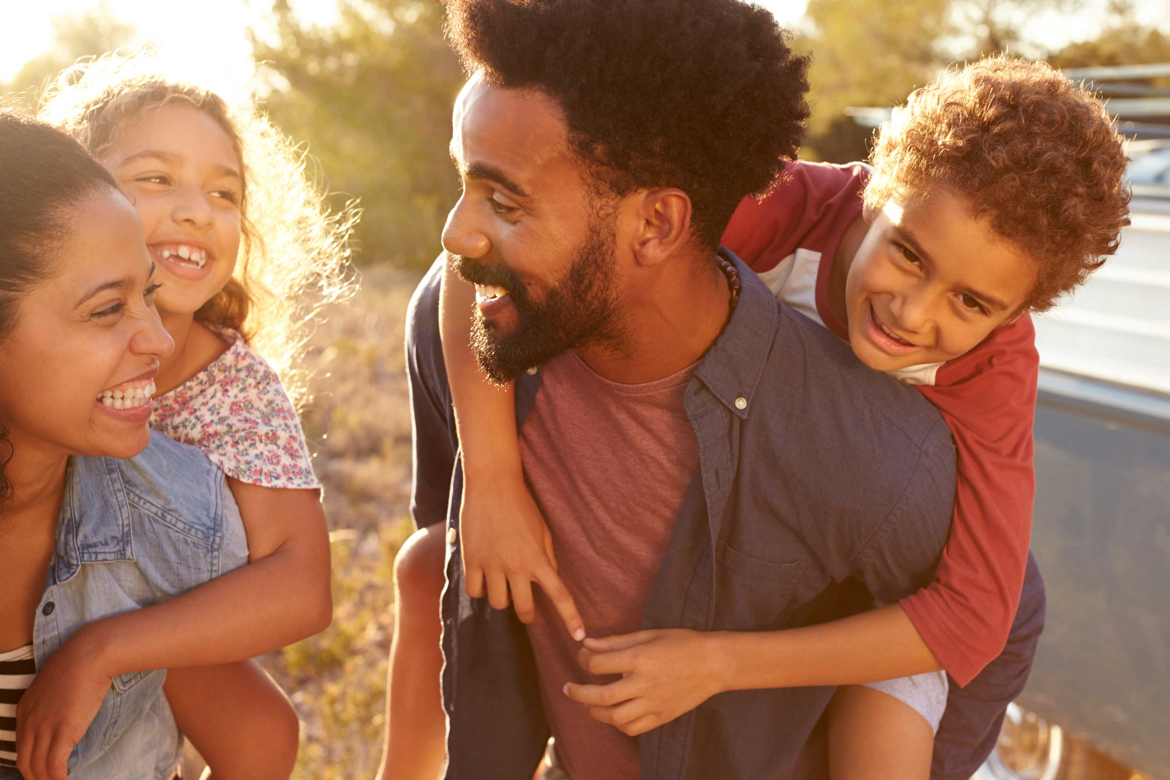 Happy diverse family enjoying sunset outdoors at Robins Landing in Houston Texas, father piggybacking son near pickup truck