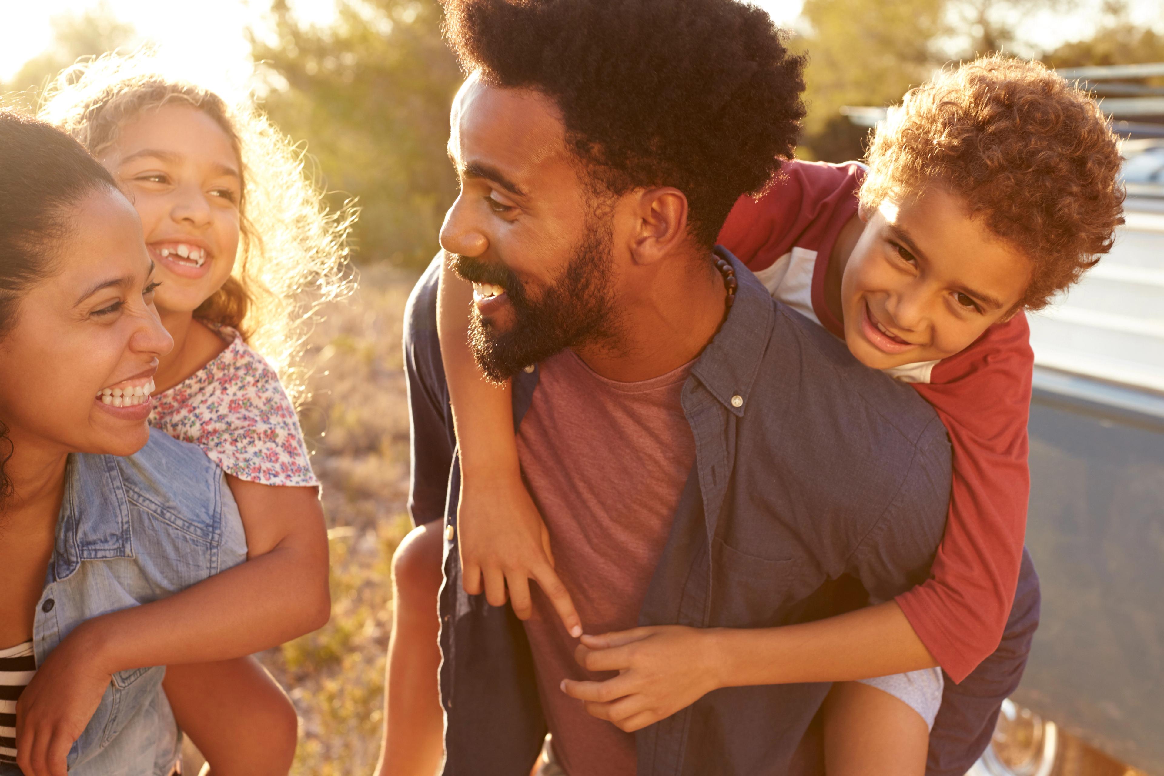 Happy diverse family enjoying sunset outdoors at Robins Landing in Houston Texas, father piggybacking son near pickup truck