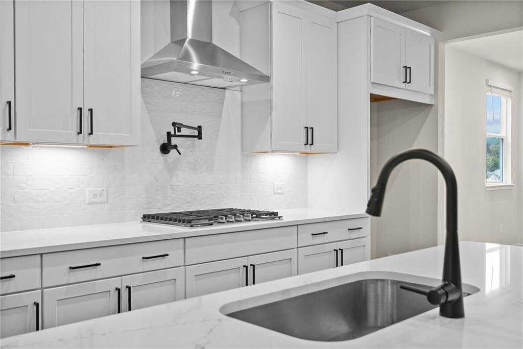 Modern white kitchen with quartz island, gas cooktop, stainless hood, black faucet in The Glenwood A, Loganville, GA