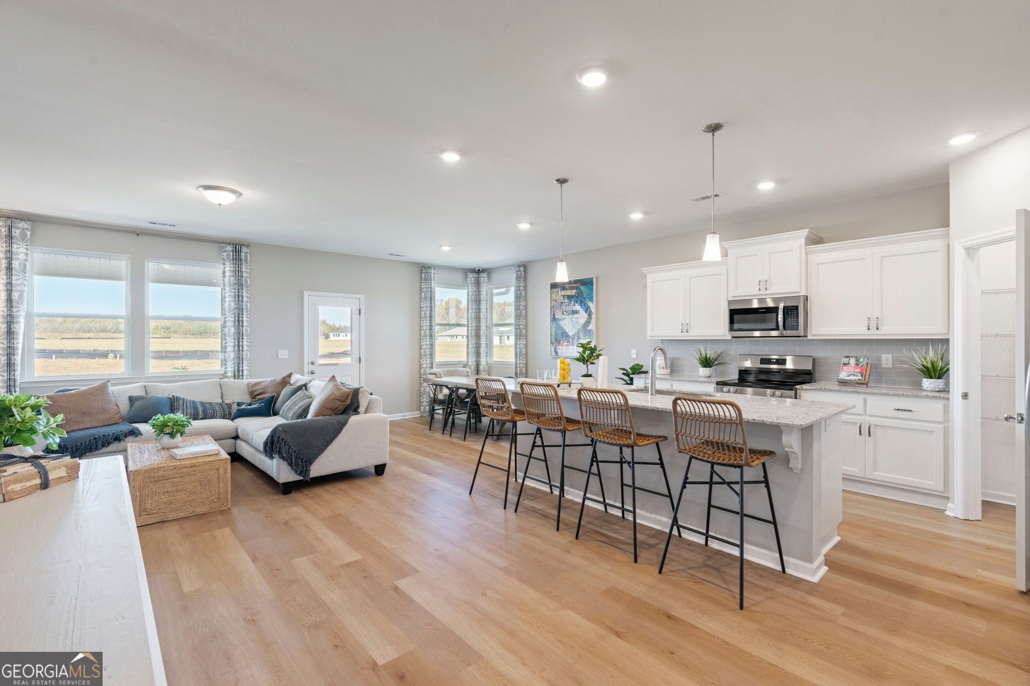 Open-concept living-kitchen with navy sectional sofa, dining table, white island bar stools, and stainless appliances in Evermore Homes The Phoenix, Perry, GA