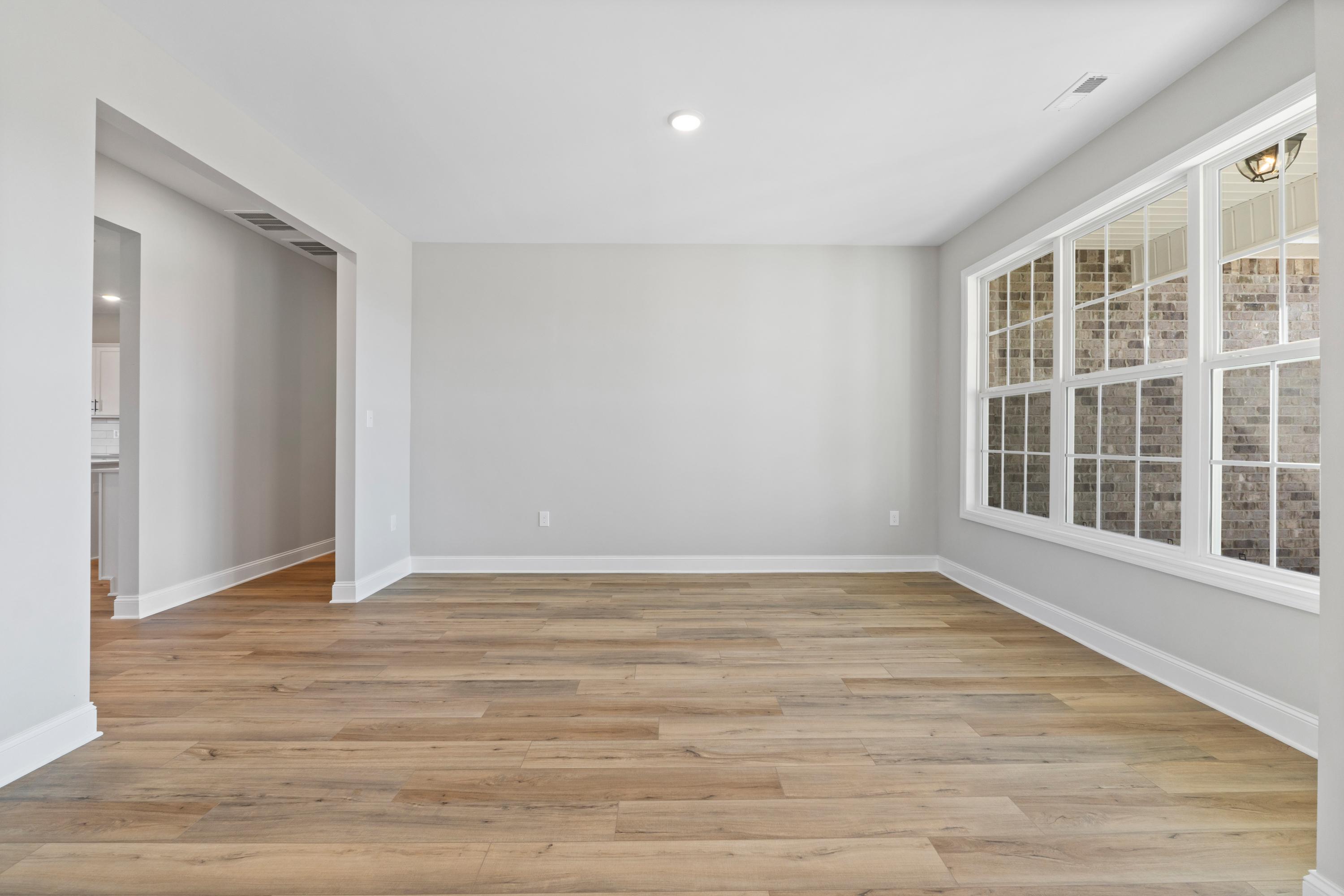 Spacious Valencia home interior with light gray walls, warm hardwood floors, large windows framing brick exterior, open archways