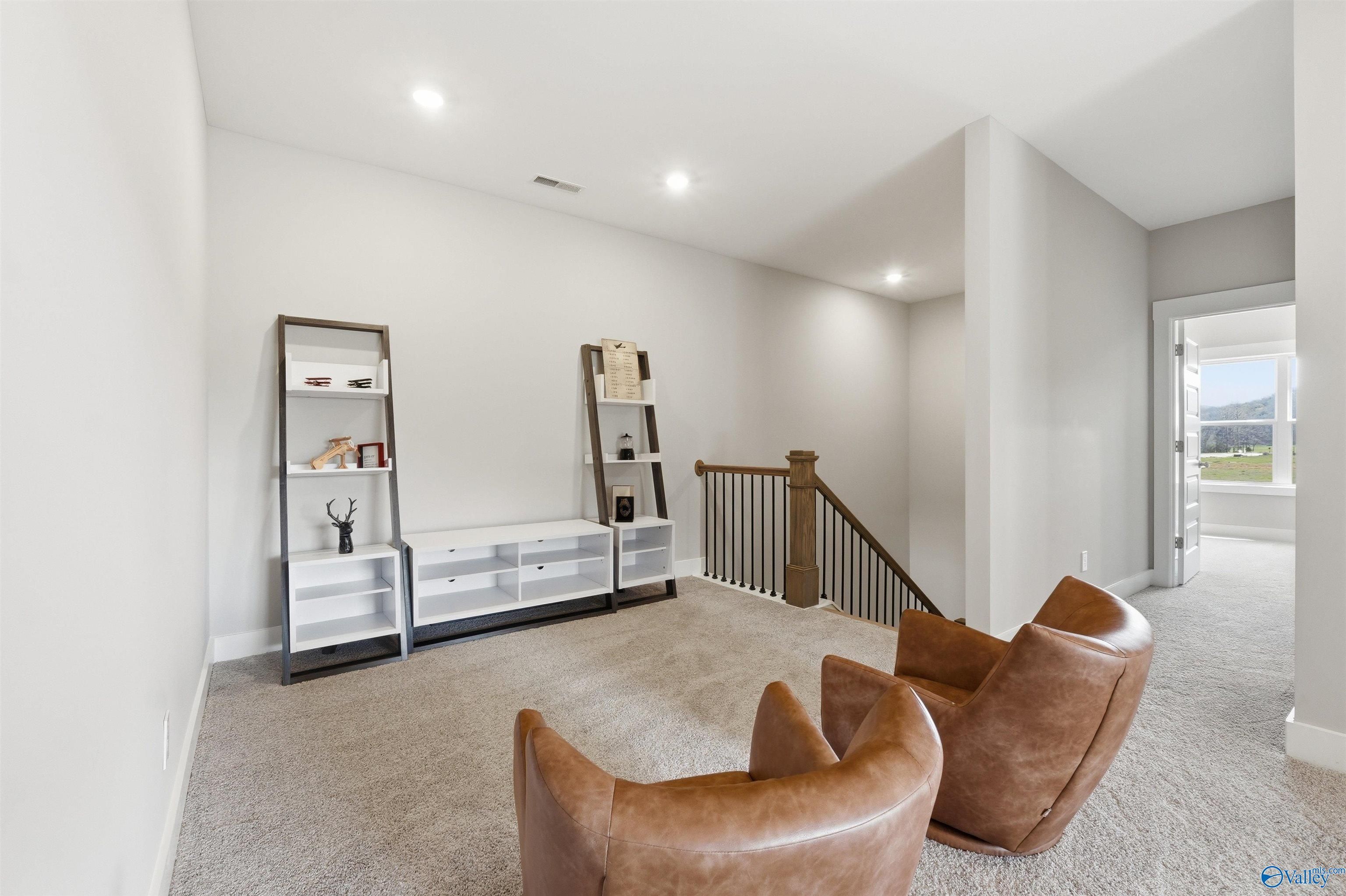 Cozy upstairs loft with ladder bookshelf, leather armchairs, oak staircase in Evermore Homes The Oxford B, Owens Cross Roads, Alabama