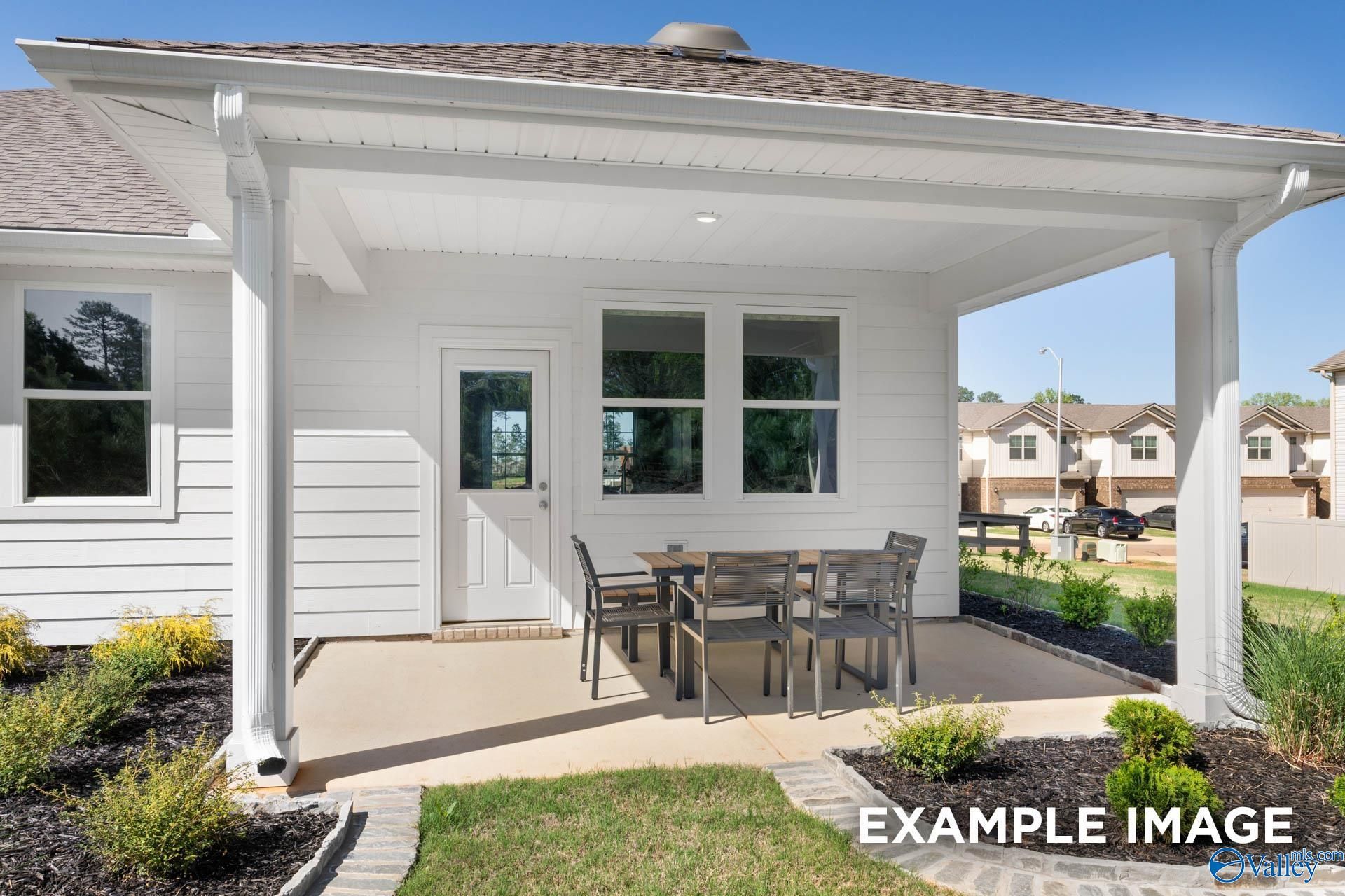 Covered patio with wicker table and chairs, white columns, and backyard greenery in Davidson Homes The Stella, Madison, Alabama