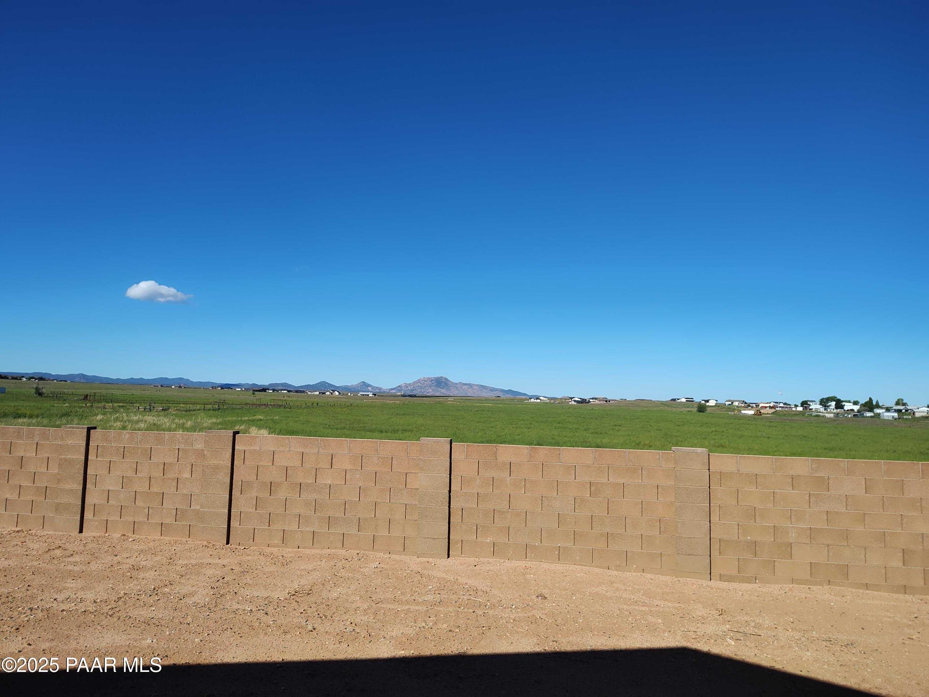 Expansive green field and distant mountain views from backyard with tan block fence in Prescott Valley, Arizona home