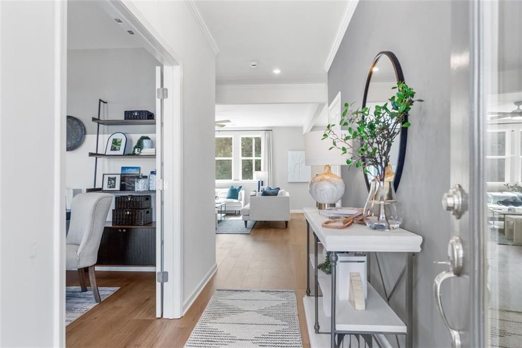 Elegant foyer with console table, large round mirror, and greenery leading to home office and living room in Davidson Homes Hickory B, Hoschton, GA