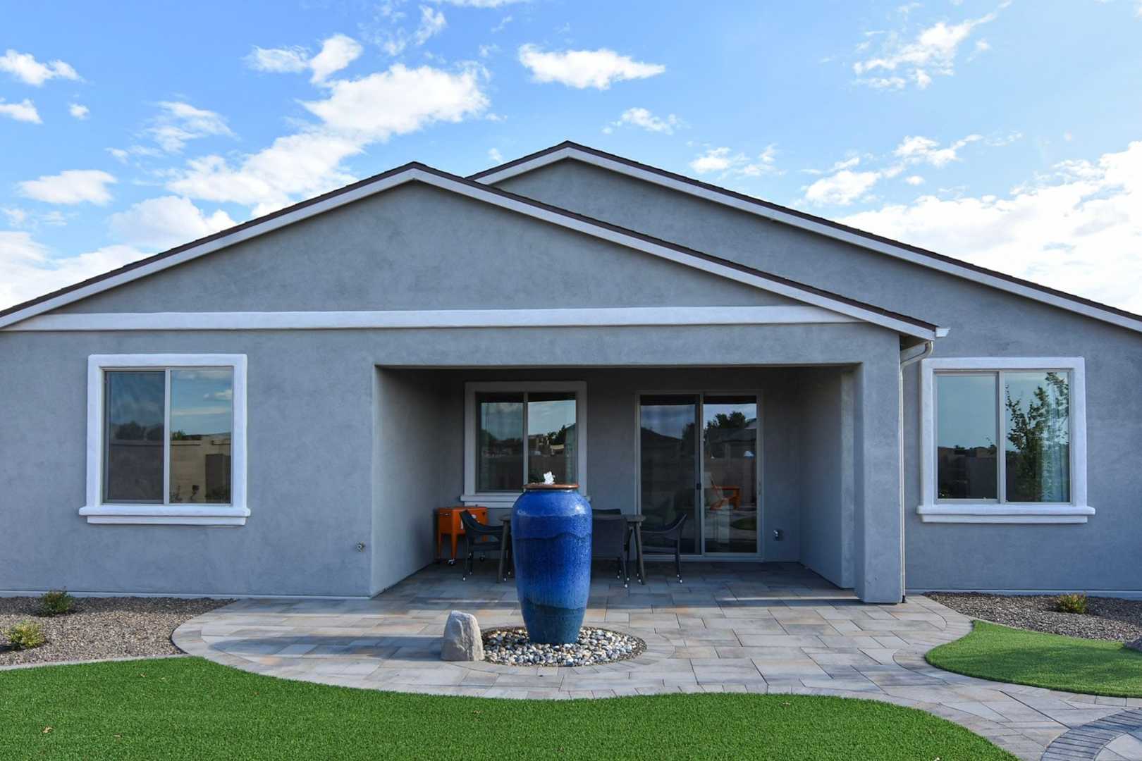Backyard patio of The Harmony single-story home with covered seating area, large sliding doors, blue vase, and desert landscaping in Prescott Valley