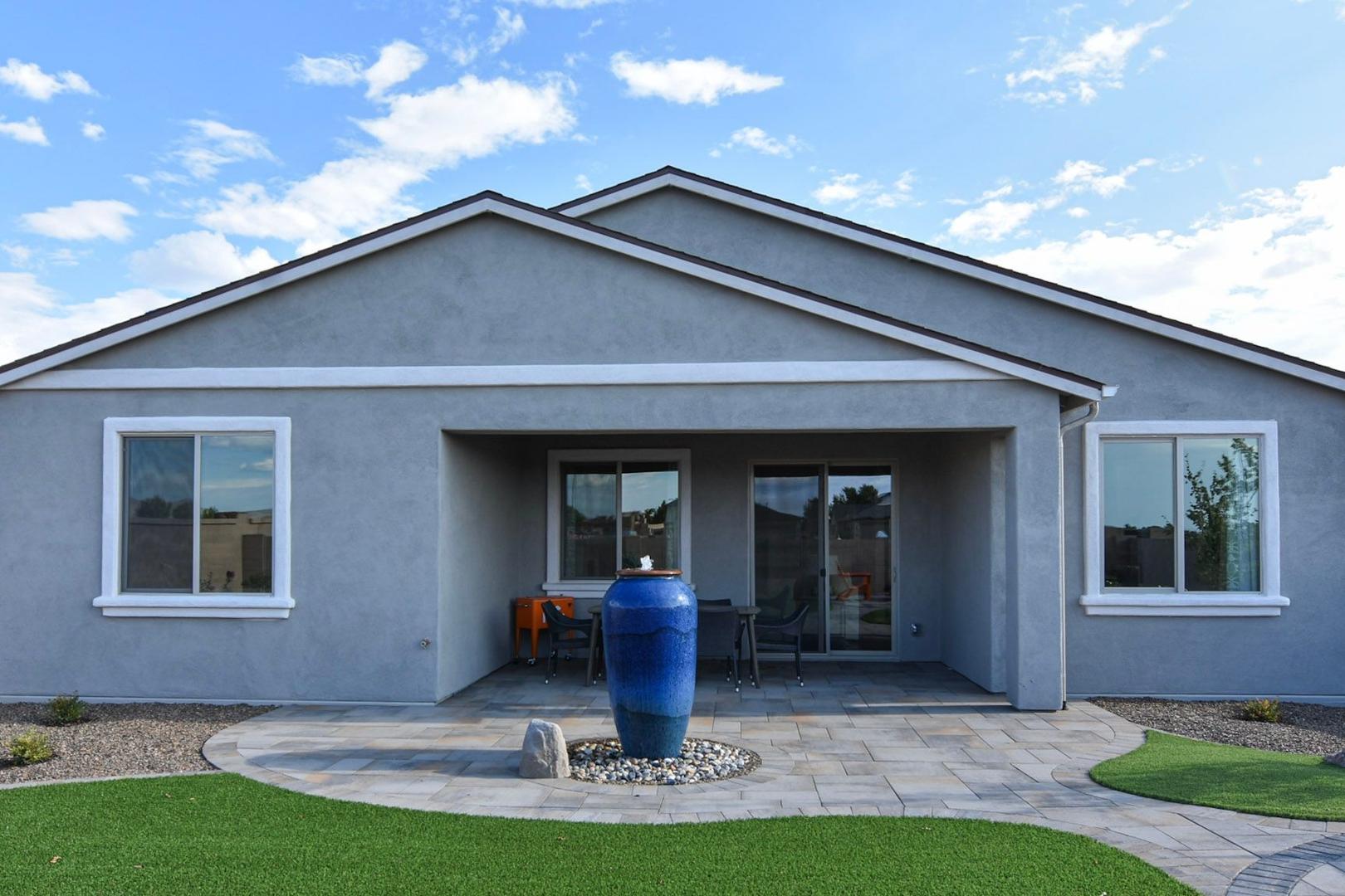 Backyard patio of The Harmony single-story home with covered seating area, large sliding doors, blue vase, and desert landscaping in Prescott Valley