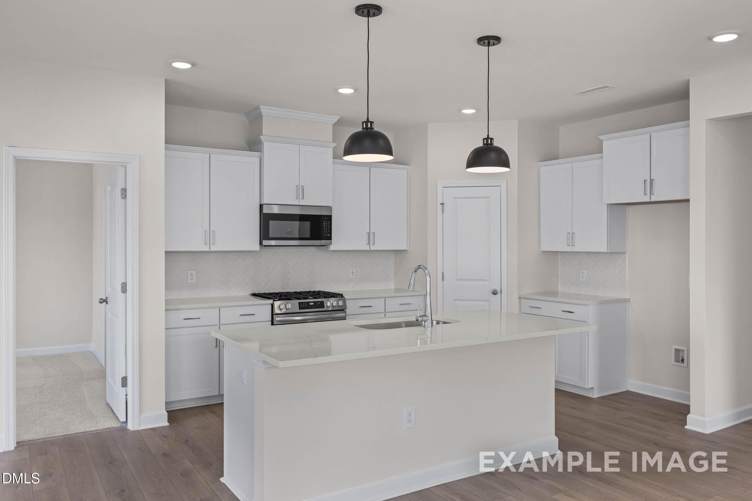 Modern kitchen with white cabinets, quartz island, and pendant lighting in The Franklin C home at Retreat at North Main.