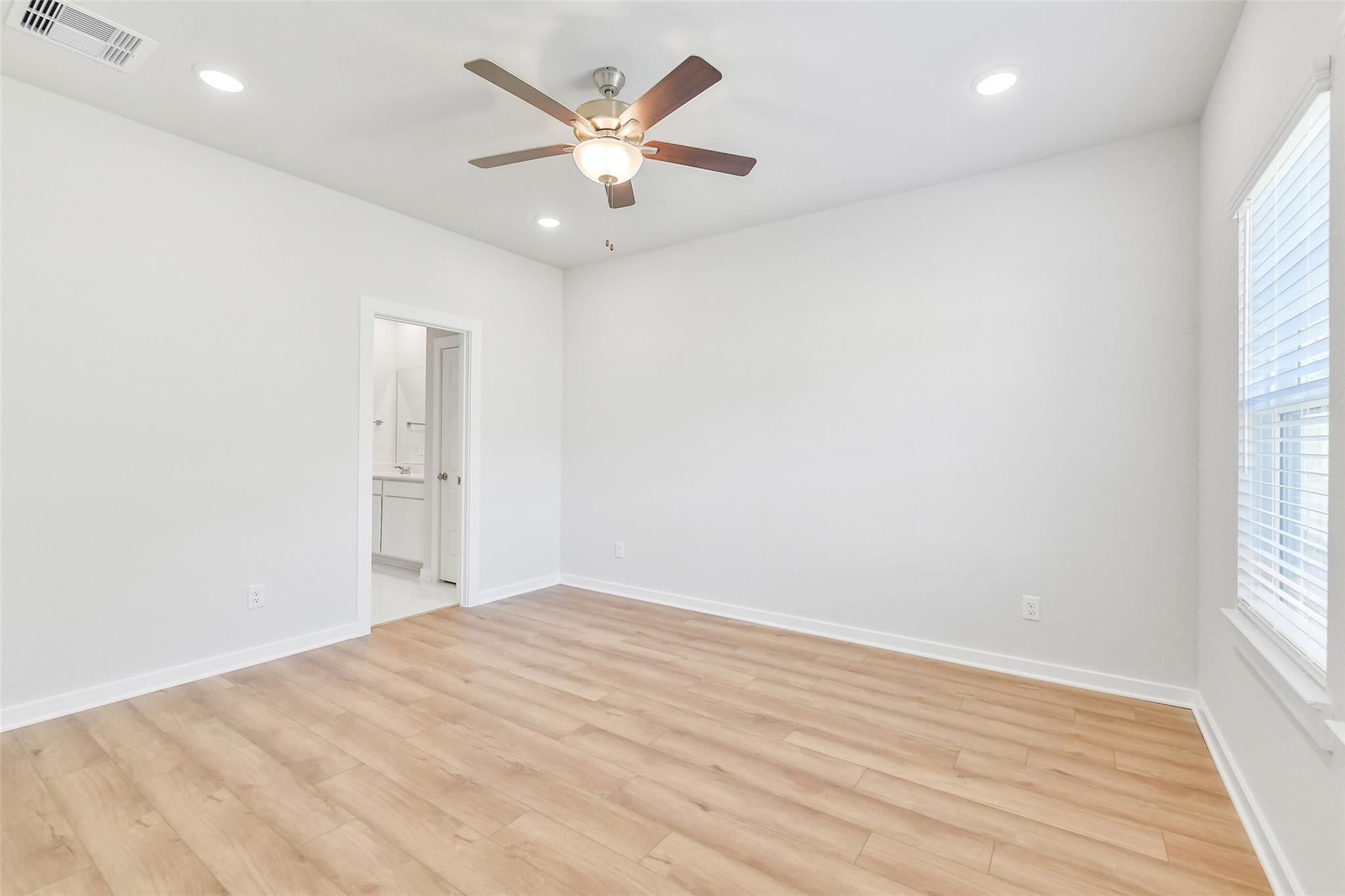 Bright master bedroom with ceiling fan, en-suite bath, and oak floors in Davidson Homes The Blanco E, Magnolia, Texas