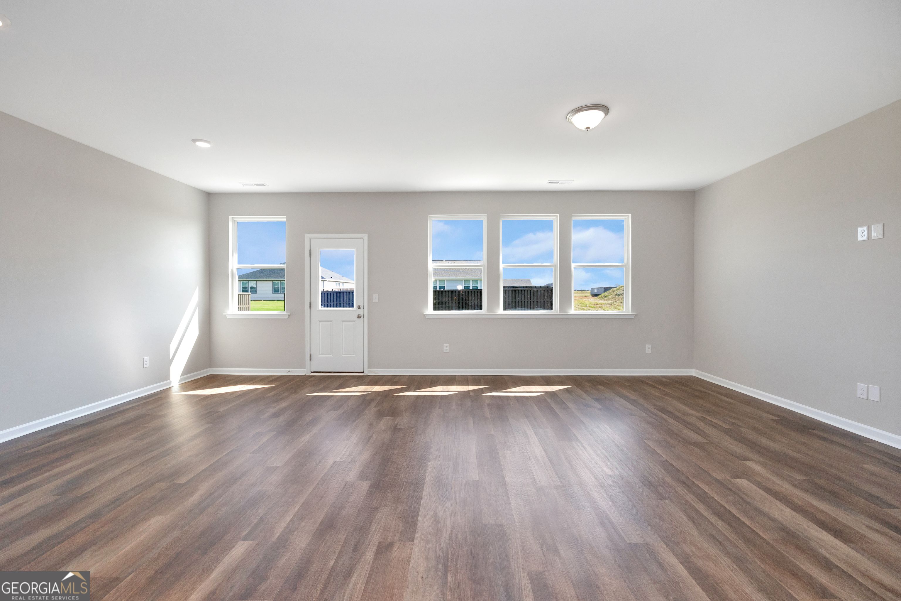 Bright living room with large windows, hardwood floors, and gray walls in Evermore Homes The Luna, Ivy Glen, Perry, Georgia