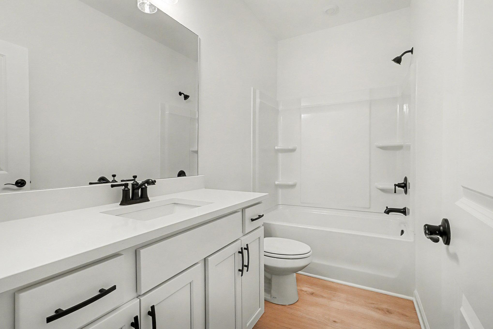 Modern guest bathroom with white vanity, tub-shower combo, and tree-view window in 4-bedroom Davidson Homes The Daphne B, Loganville, GA