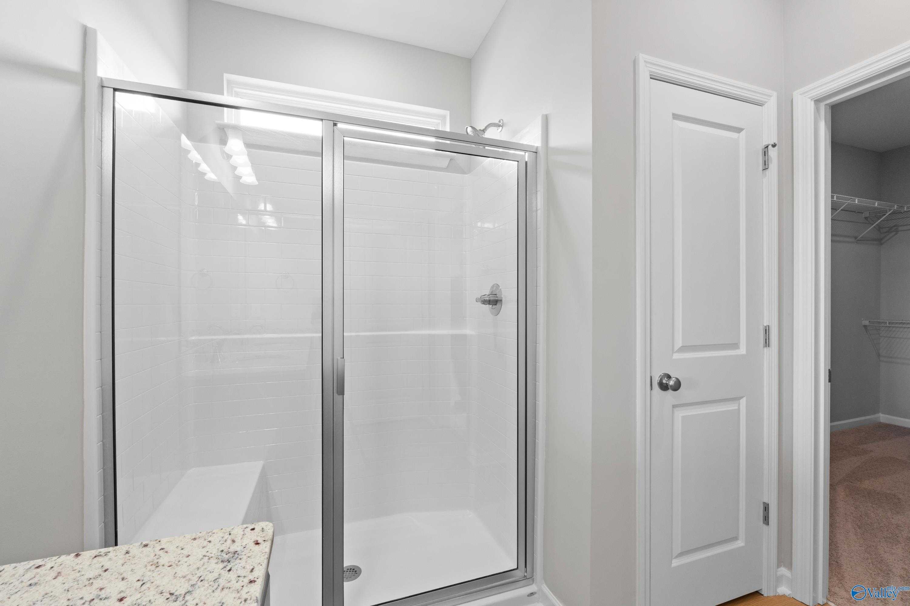 Modern master bathroom featuring frameless glass walk-in shower, quartz vanity, and adjacent closet in Evermore Homes The Aurora, Harvest, AL