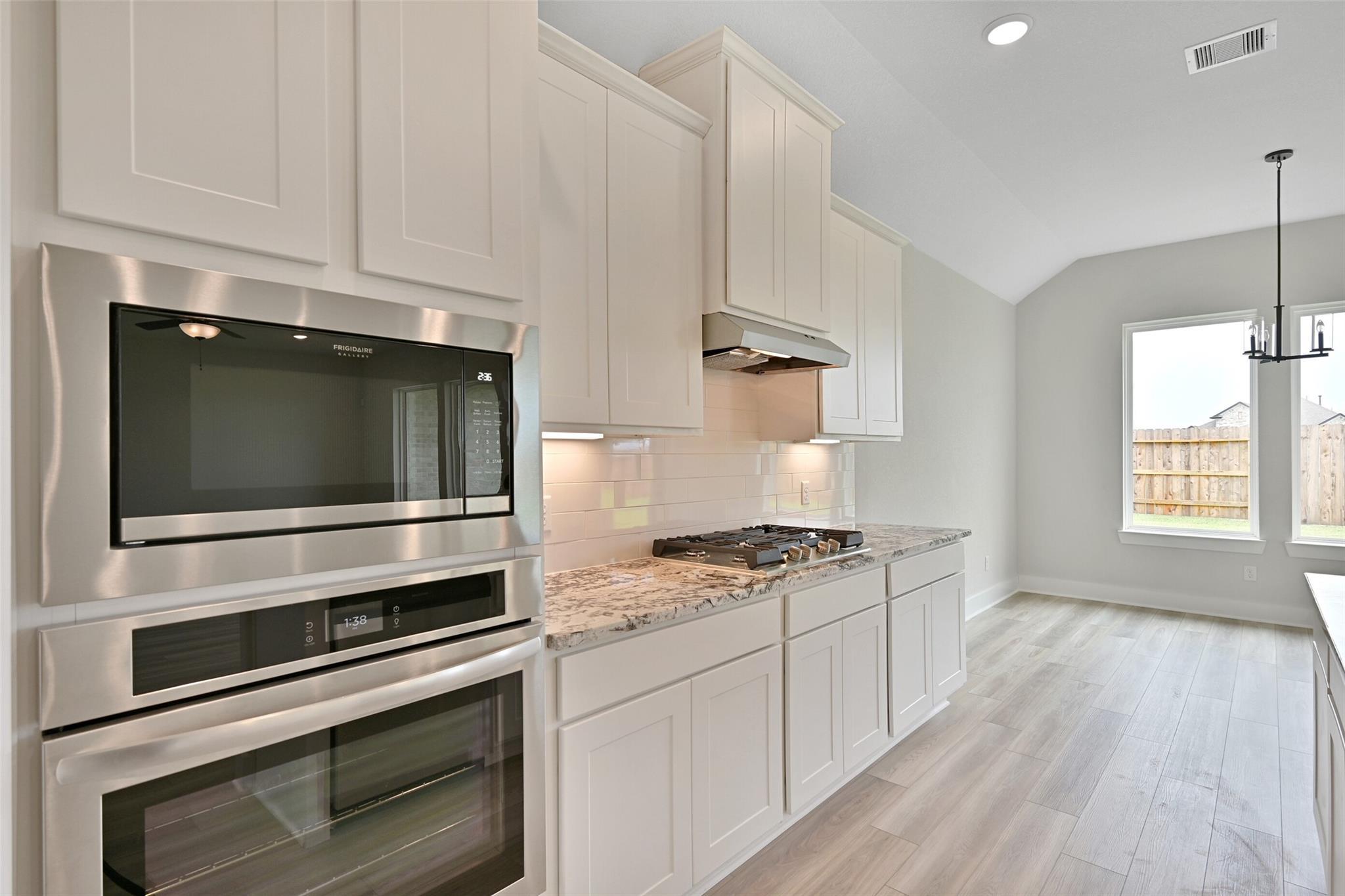 Modern white shaker kitchen with stainless double ovens, granite counters, and island in Davidson Homes The Edward C, Lago Mar, Texas City