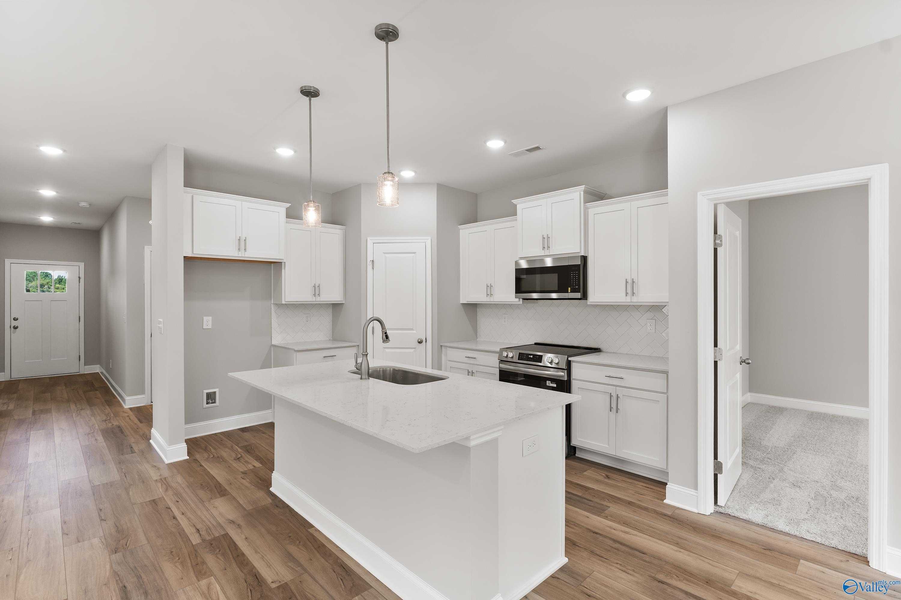 Modern white shaker kitchen with quartz island sink, stainless appliances, pendant lights in Davidson Homes Franklin C, Toney, AL