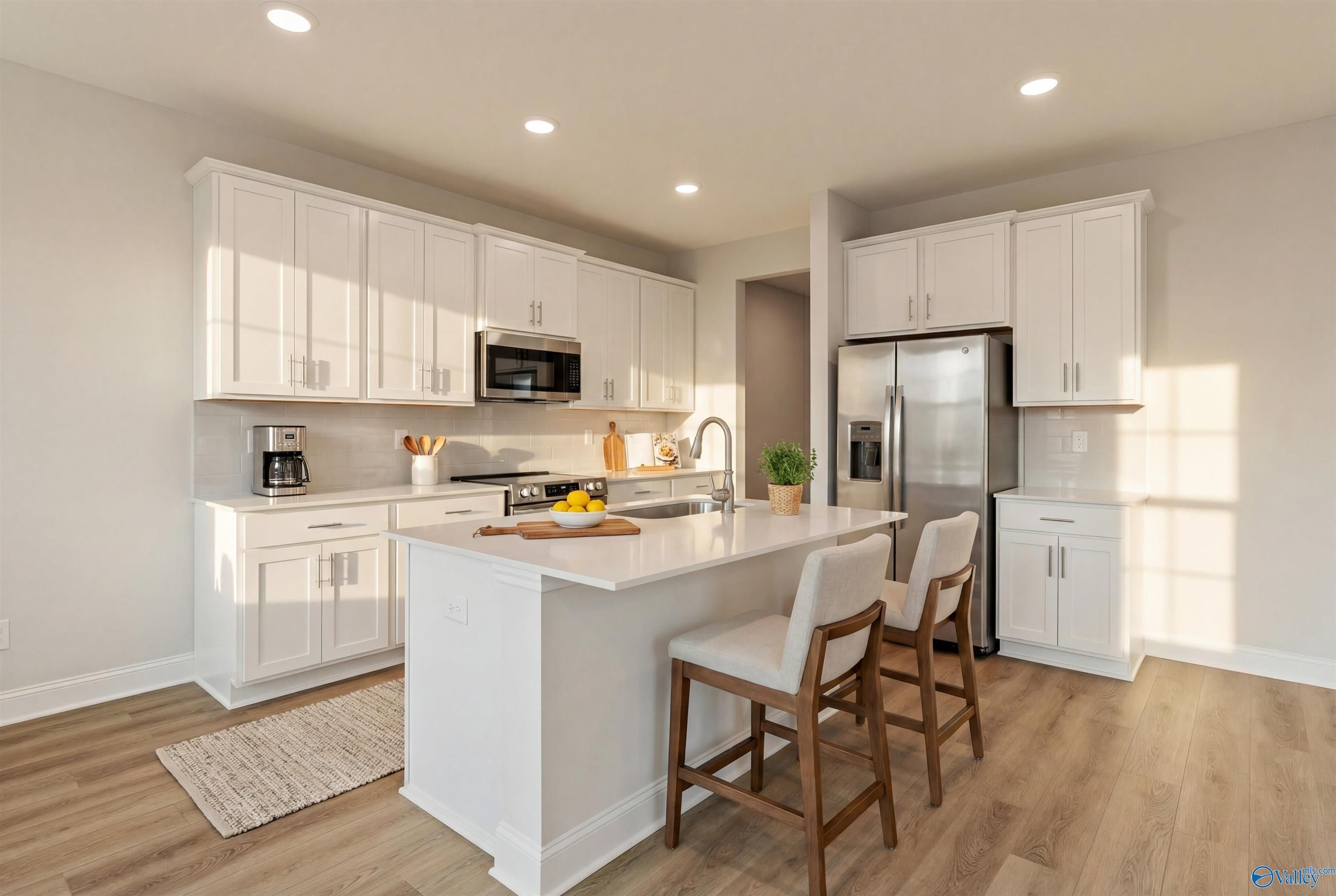 Modern white kitchen with central island, stainless appliances, bar stools in Davidson Homes The Camden, Huntsville, Alabama