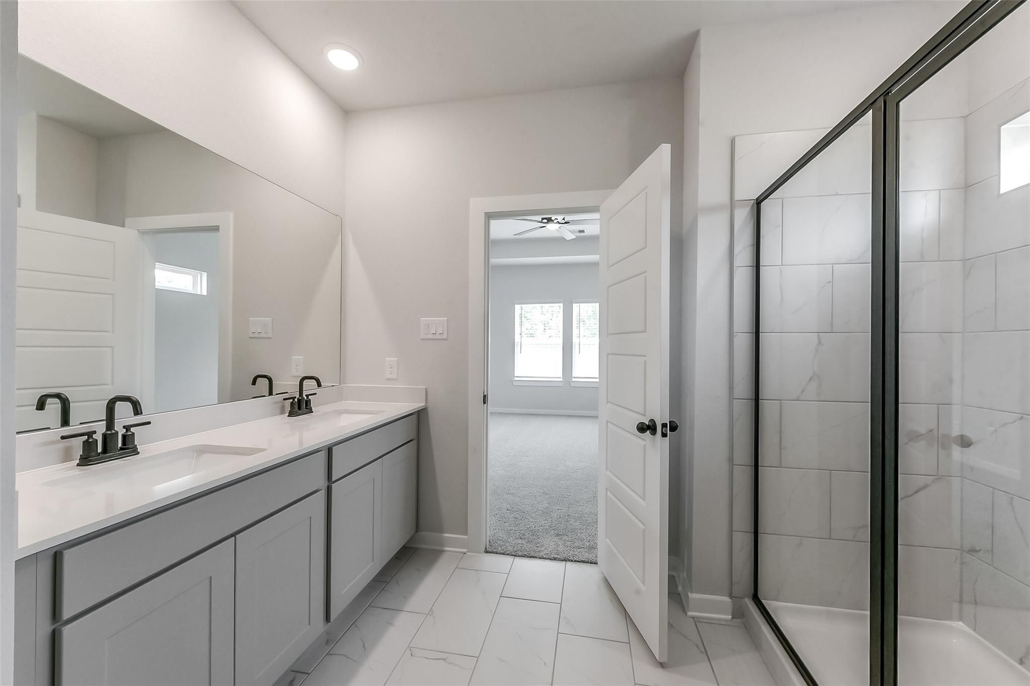 Elegant master bathroom with double gray vanity, quartz counters, black faucets, and frameless glass shower in Davidson Homes Everett C, Crosby TX