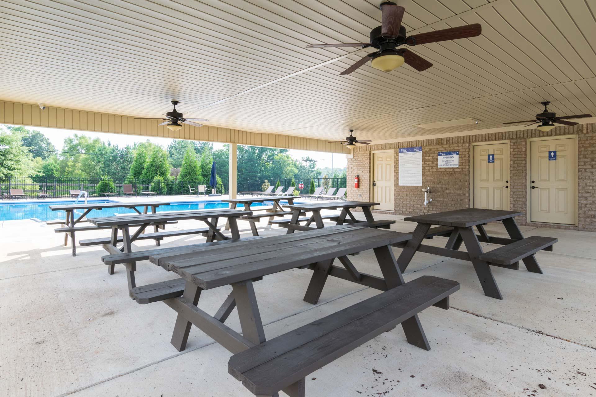 Covered pavilion with wooden picnic tables and ceiling fans at Ivy Hills in Toney, Alabama, overlooking community pool