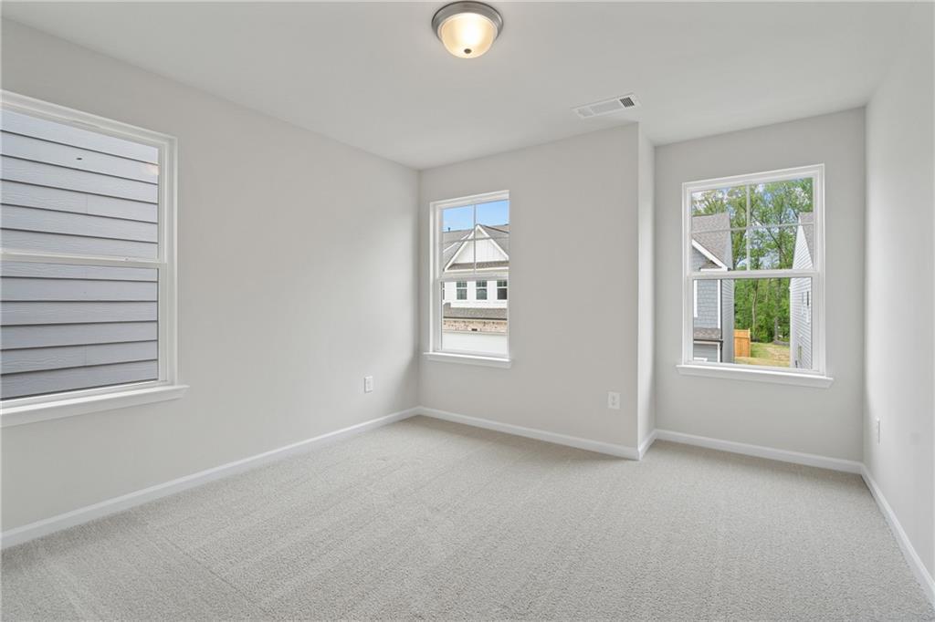 Bright empty bedroom with light gray walls, beige carpet, and large windows overlooking neighborhood in Davidson Homes The Marion B, Kennesaw, Georgia