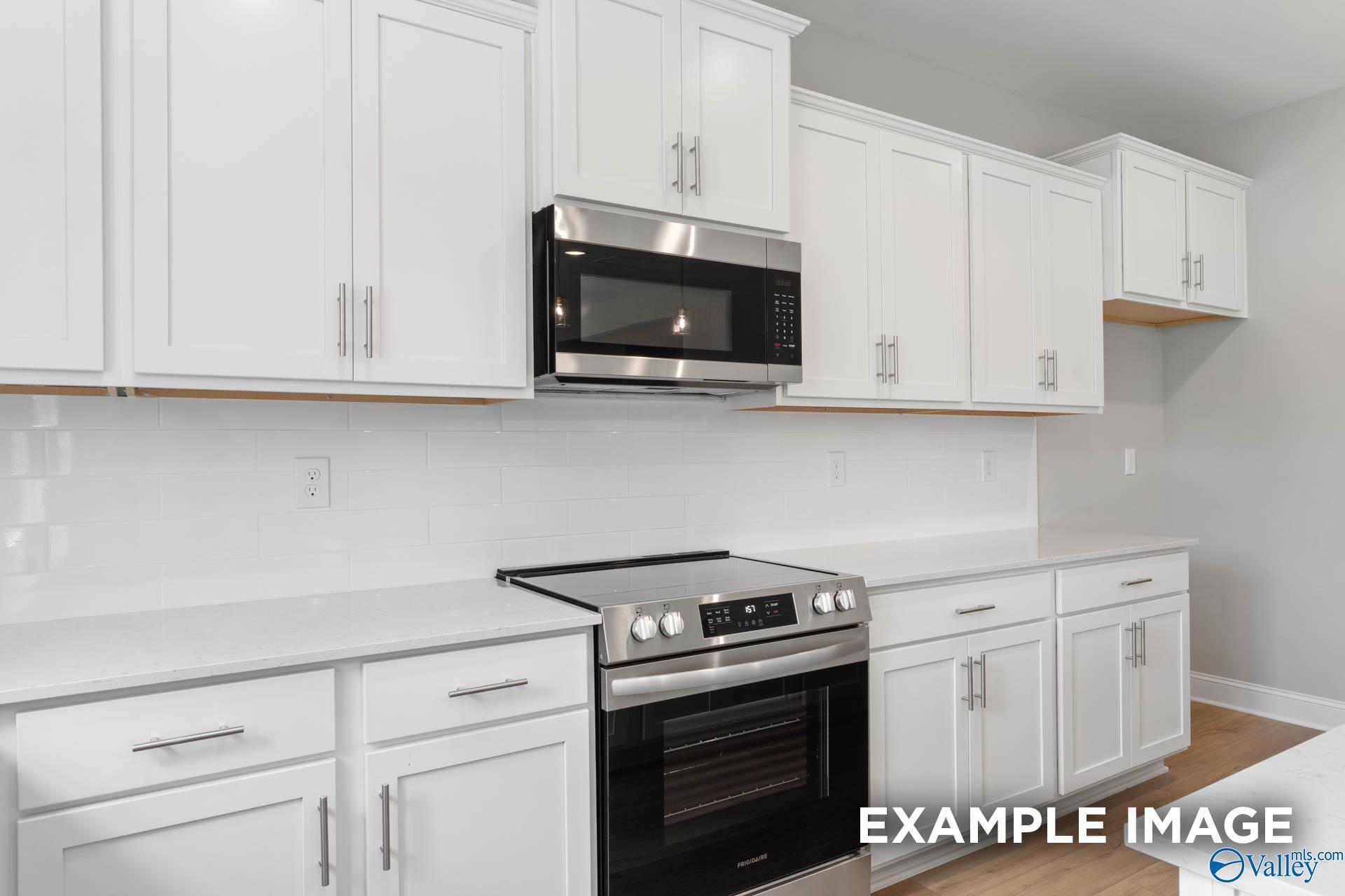 Modern kitchen with white shaker cabinets, quartz countertops, and stainless appliances in The Chelsea B at Wood Trail.