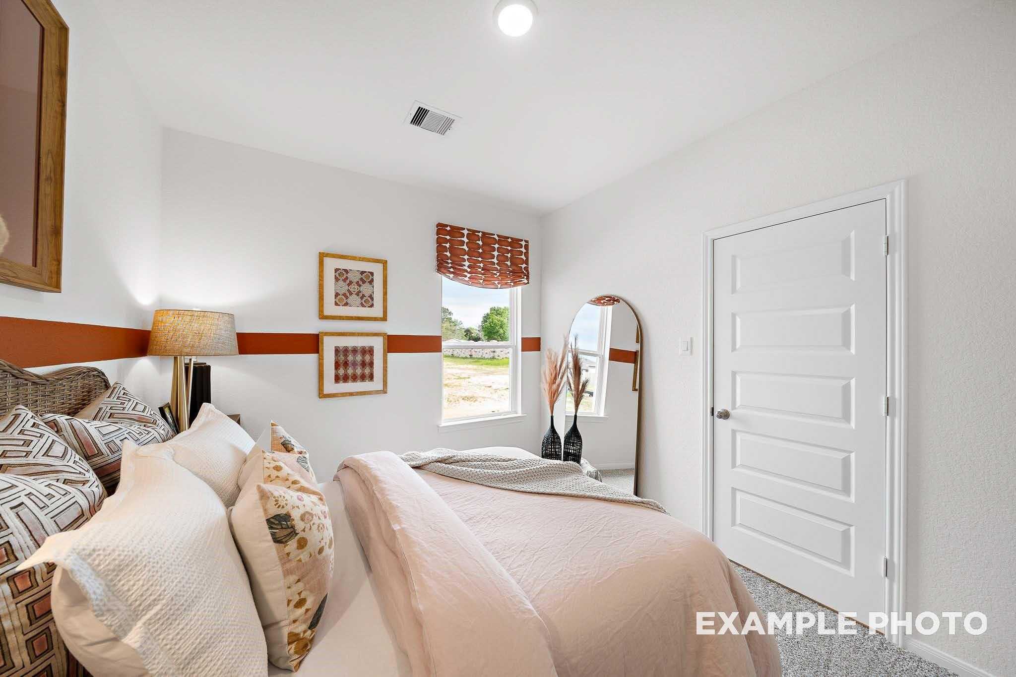 Cozy secondary bedroom featuring queen bed with neutral bedding, floor lamp, full-length mirror, and window view in Davidson Homes The Sabine F, Magnolia, Texas