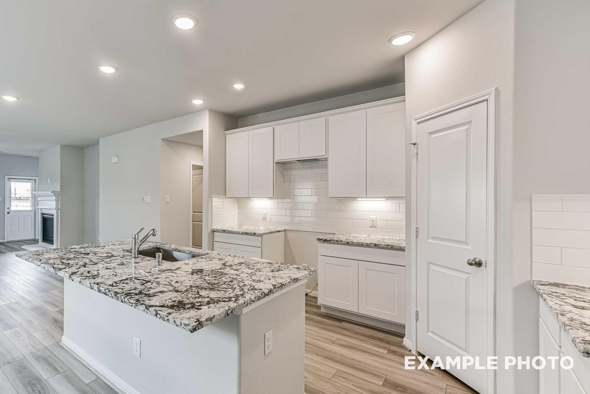 Modern white kitchen with granite island sink, subway tile backsplash, and open layout in Davidson Homes The Riviera A, Rosharon, Texas