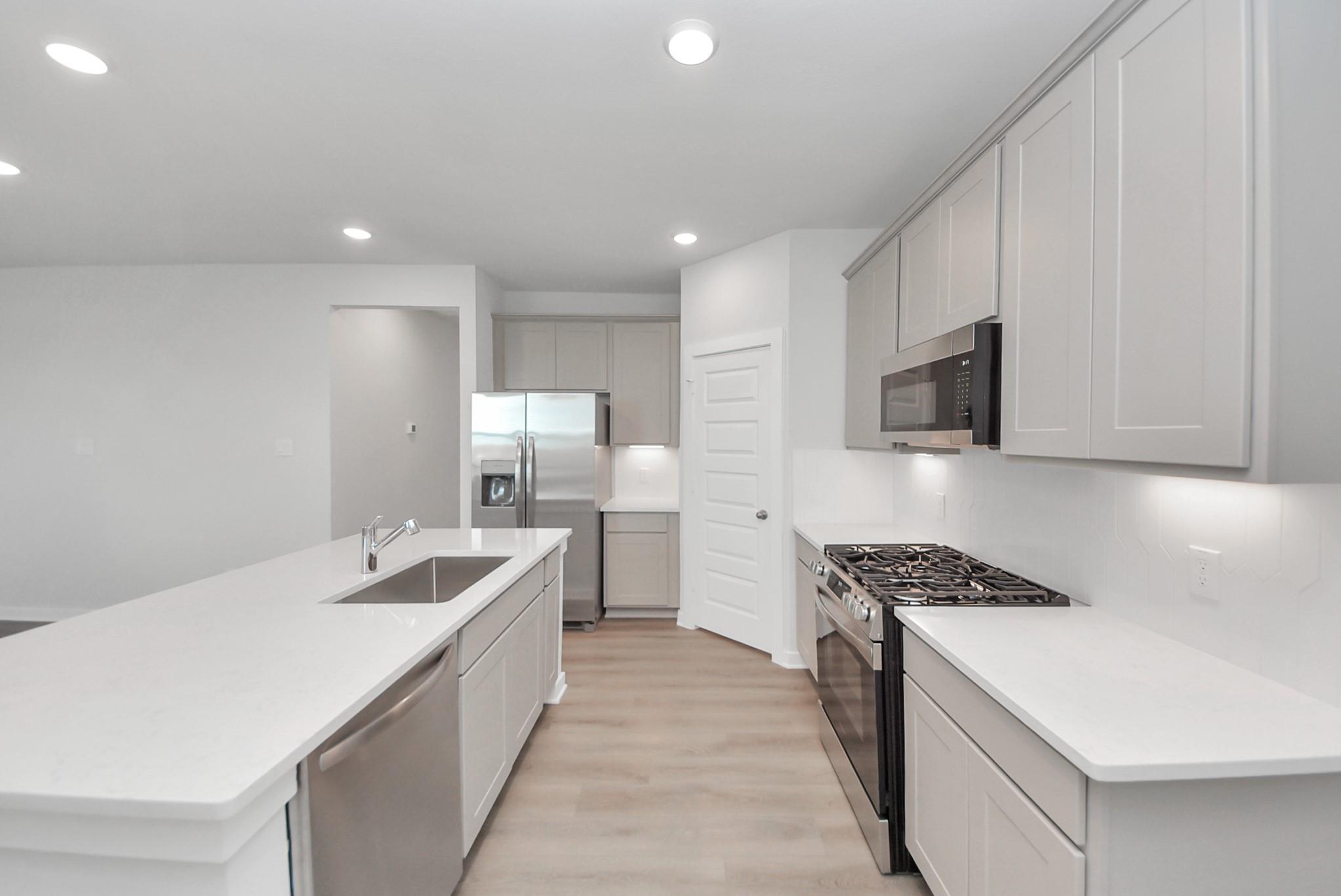 Modern kitchen with white quartz island, gas cooktop, and stainless appliances in Davidson Homes San Marcos E, Beasley, Texas