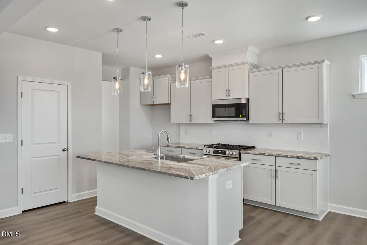 Modern white kitchen with granite island sink, stainless steel range and microwave, pendant lights in Davidson Homes The Willow G, Angier NC