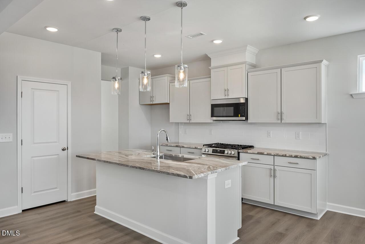 Modern white kitchen with granite island sink, stainless steel range and microwave, pendant lights in Davidson Homes The Willow G, Angier NC