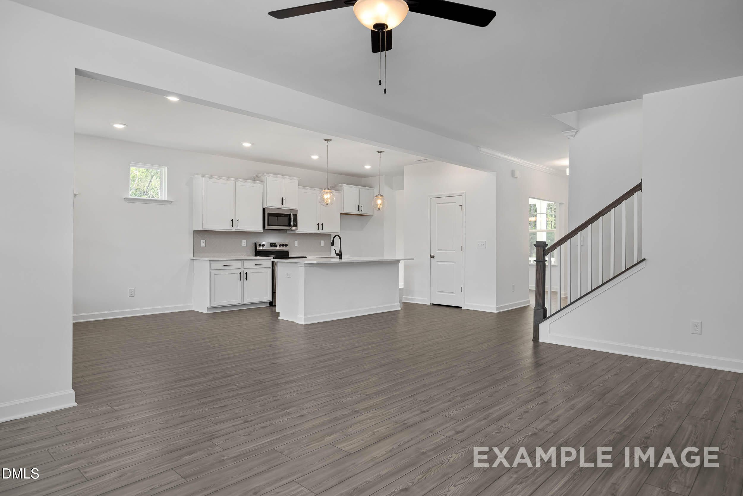 Open-concept kitchen and living area with white cabinetry, large island, hardwood floors, and staircase in Davidson Homes The Willow D, Zebulon, NC
