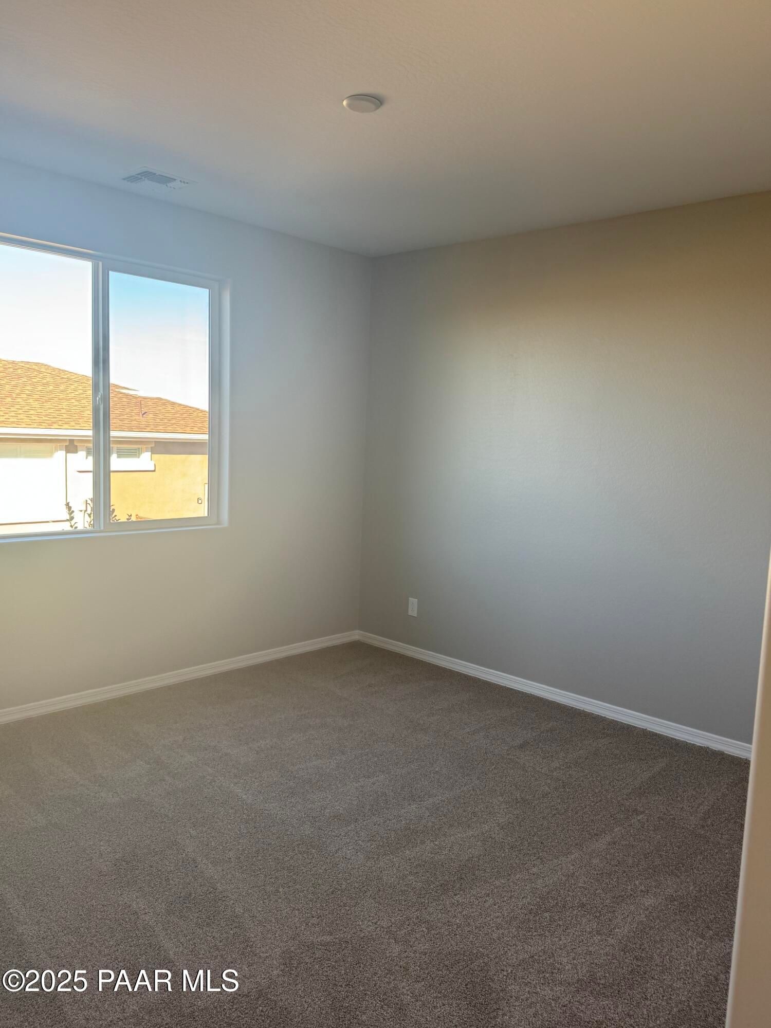 Bright empty bedroom with neutral beige walls, large sunny window, and plush carpet in Davidson Homes The Monarch E, Prescott, Arizona