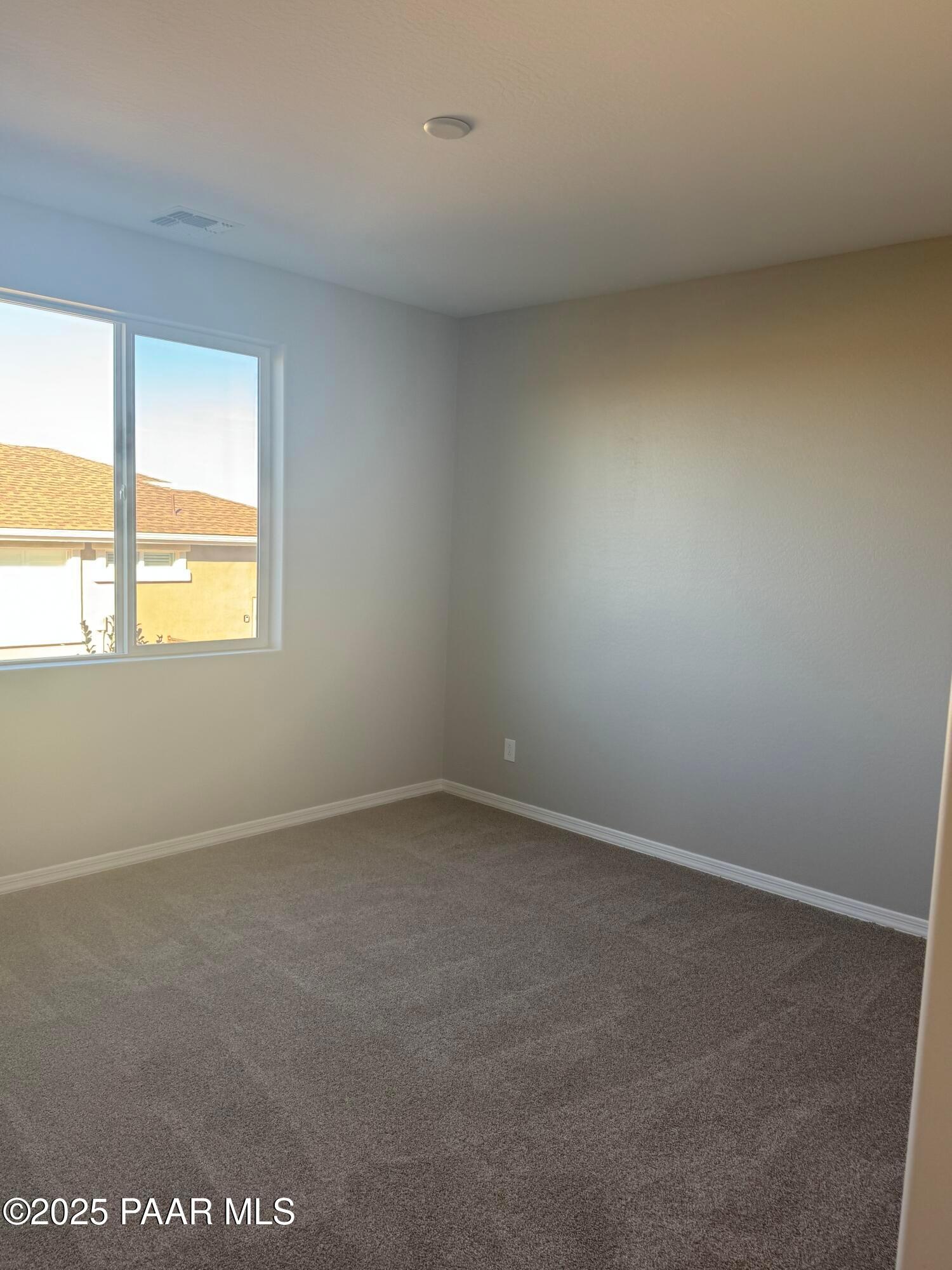 Bright empty bedroom with neutral beige walls, large sunny window, and plush carpet in Davidson Homes The Monarch E, Prescott, Arizona