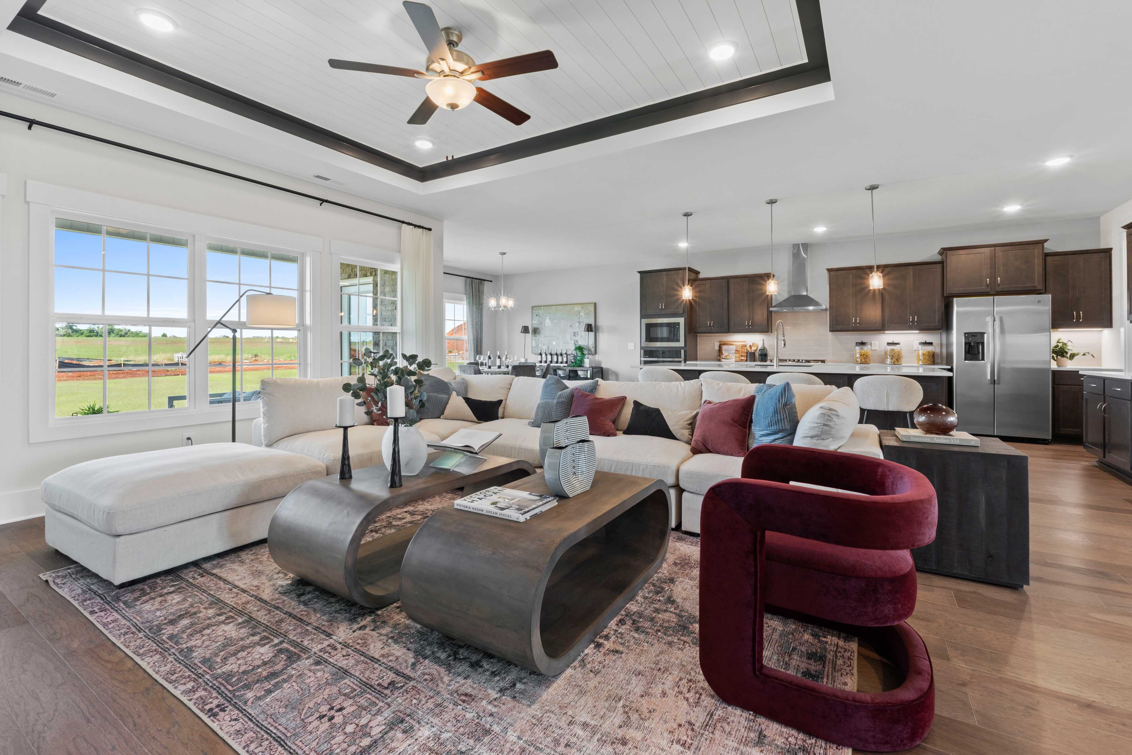 Spacious open-concept living room and kitchen at Creekside in Harvest Alabama featuring white L-shaped sofa hardwood floors dark cabinets and large windows