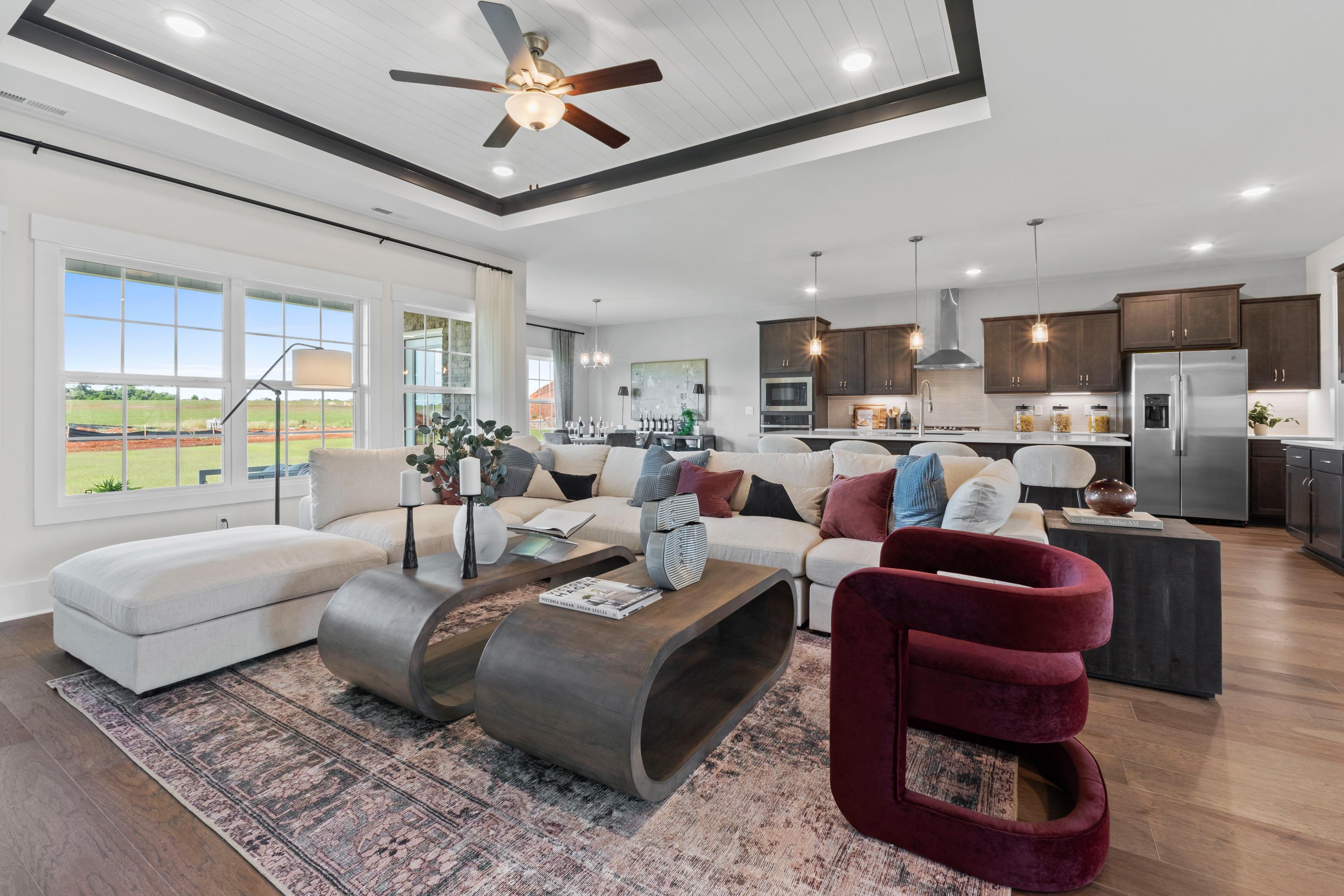 Spacious open-concept living room and kitchen at Creekside in Harvest Alabama featuring white L-shaped sofa hardwood floors dark cabinets and large windows