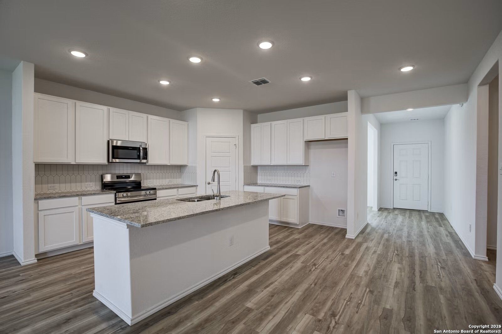 Modern white kitchen featuring granite island, stainless steel appliances, and wood flooring in Davidson Homes The Douglas B, Seguin, Texas