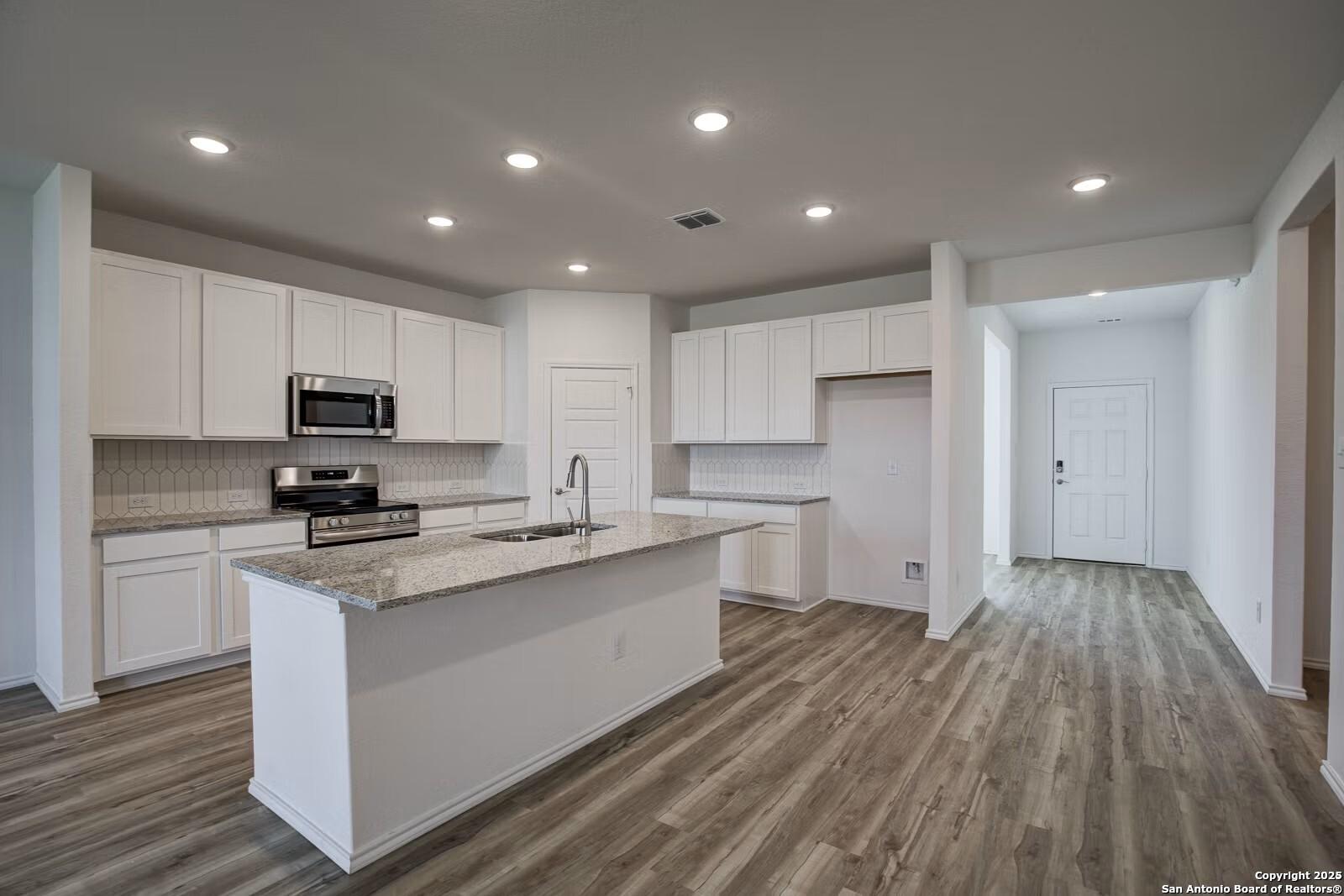 Modern white kitchen featuring granite island, stainless steel appliances, and wood flooring in Davidson Homes The Douglas B, Seguin, Texas