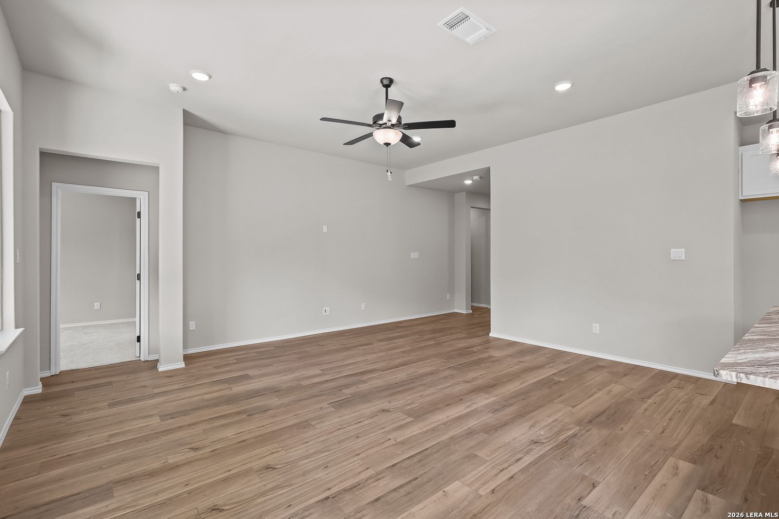 Spacious open-concept living area with wood-look flooring and ceiling fan in Davidson Homes The Sequoia C, Royal Crest San Antonio