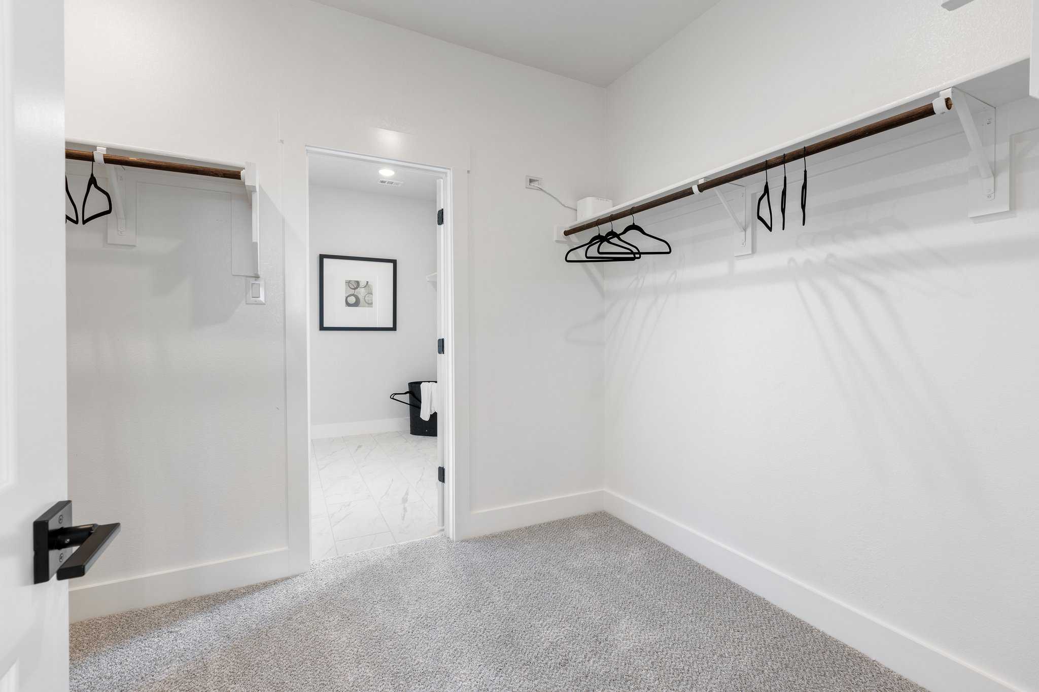 Spacious master walk-in closet in The Sequoia featuring white walls, wooden shelves, hanging rods, and open bedroom door