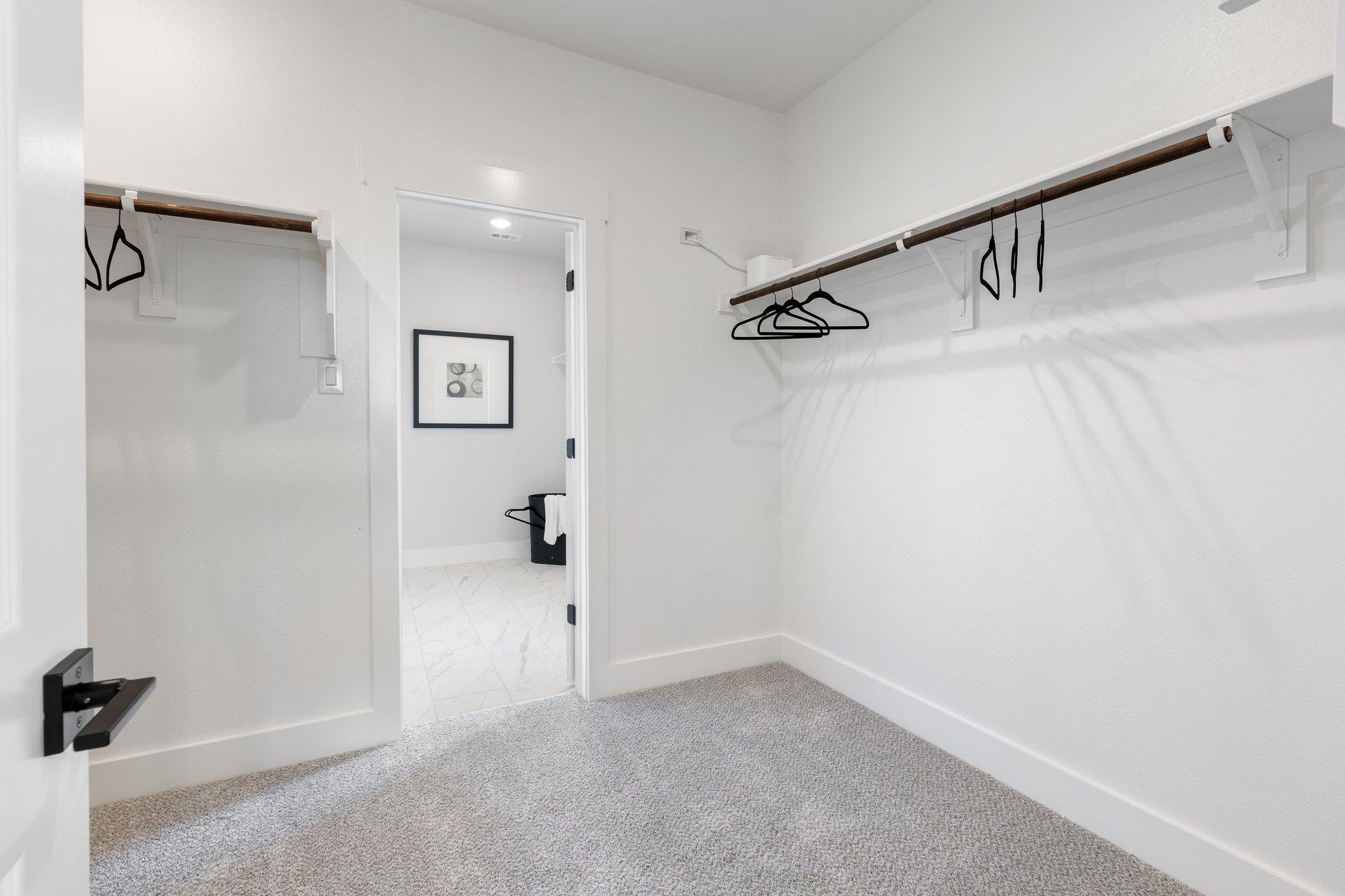 Spacious master walk-in closet in The Sequoia home with white walls, wooden shelves, hanging rods, and open bathroom door