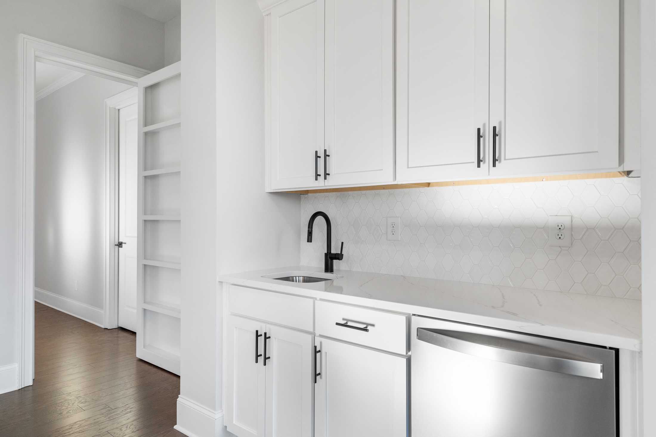 Spacious butler's pantry in The Seaside home with white shaker cabinets, black faucet sink, quartz counters, and hexagon tile backsplash