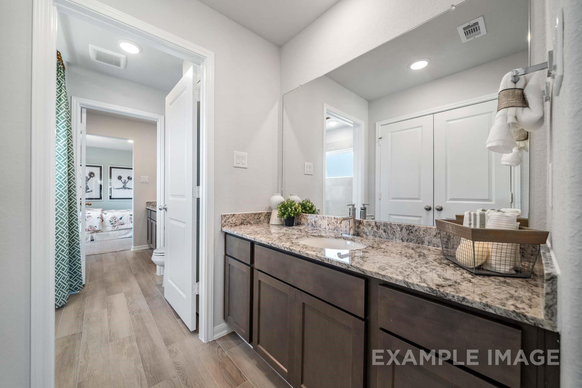 Bathroom with granite countertop vanity, dark wood cabinets, and large mirror in Davidson Homes The Acadia A floor plan, Lago Mar, Texas City