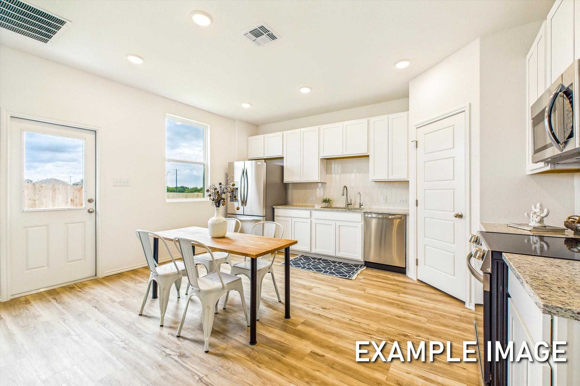 Bright kitchen in The Trinity B with white cabinets, stainless appliances, granite counters, and dining nook in San Antonio home