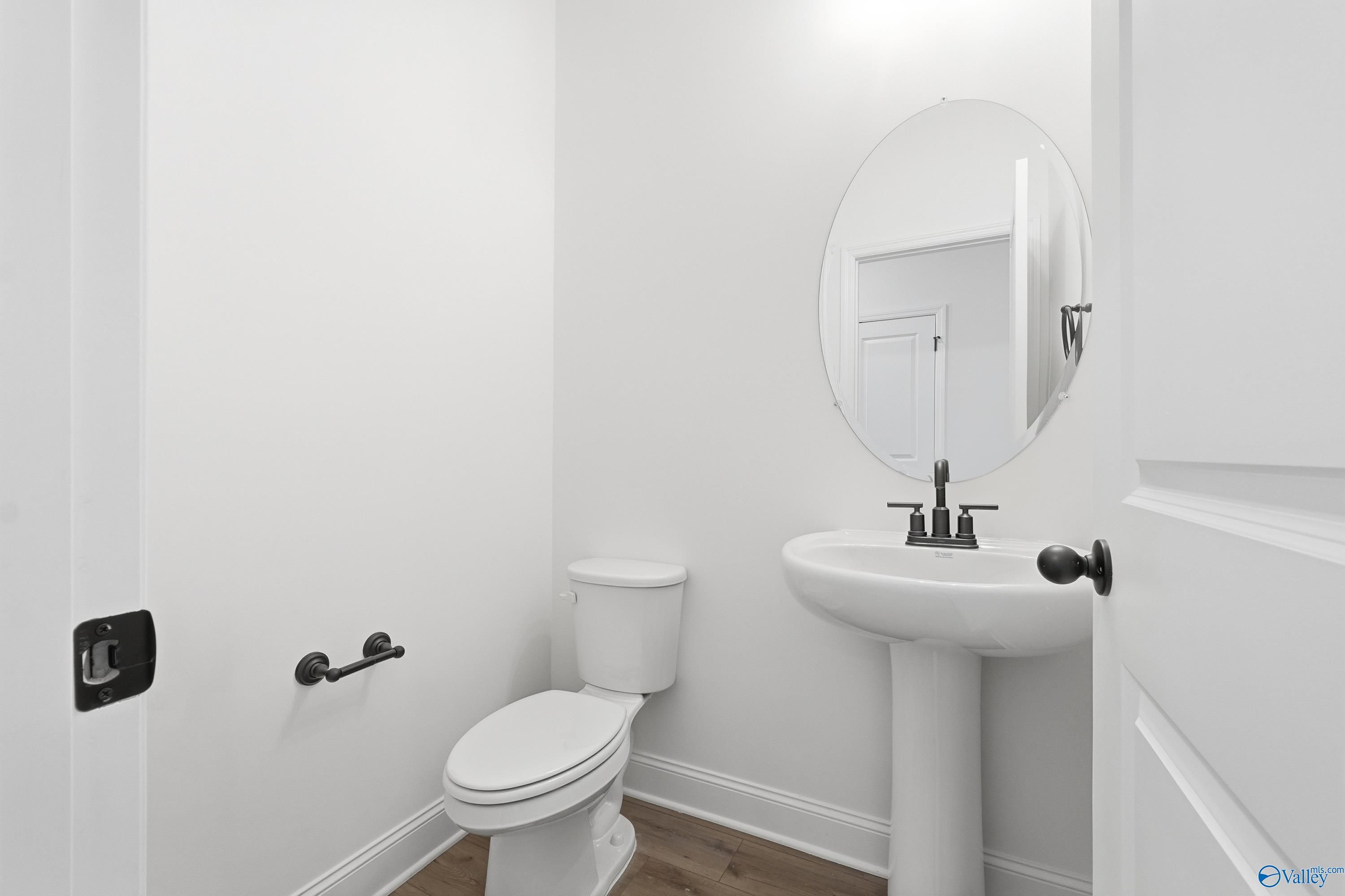 Bright powder room with pedestal sink, round mirror, and toilet in Davidson Homes The Rockford D, Hazel Green, Alabama