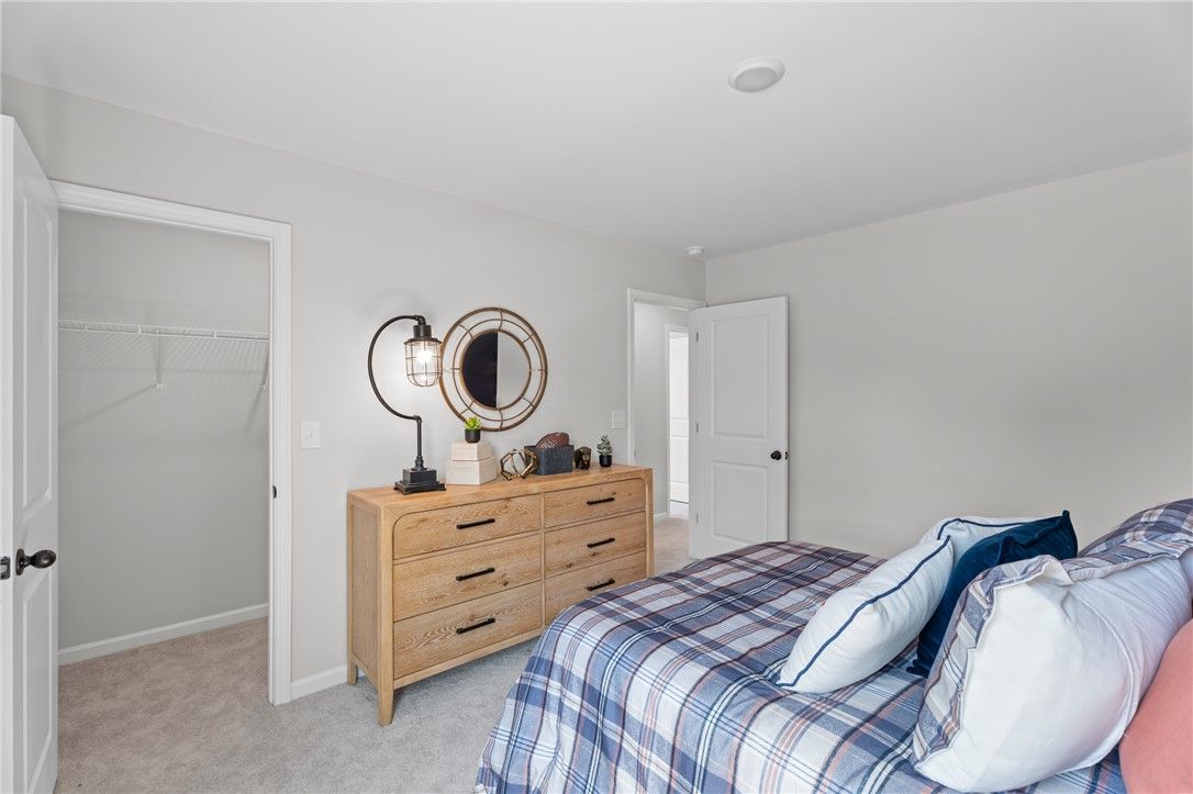 Bright bedroom with plaid bedding, wooden dresser, and walk-in closet in Davidson Homes The Stella B, Opelika, Alabama